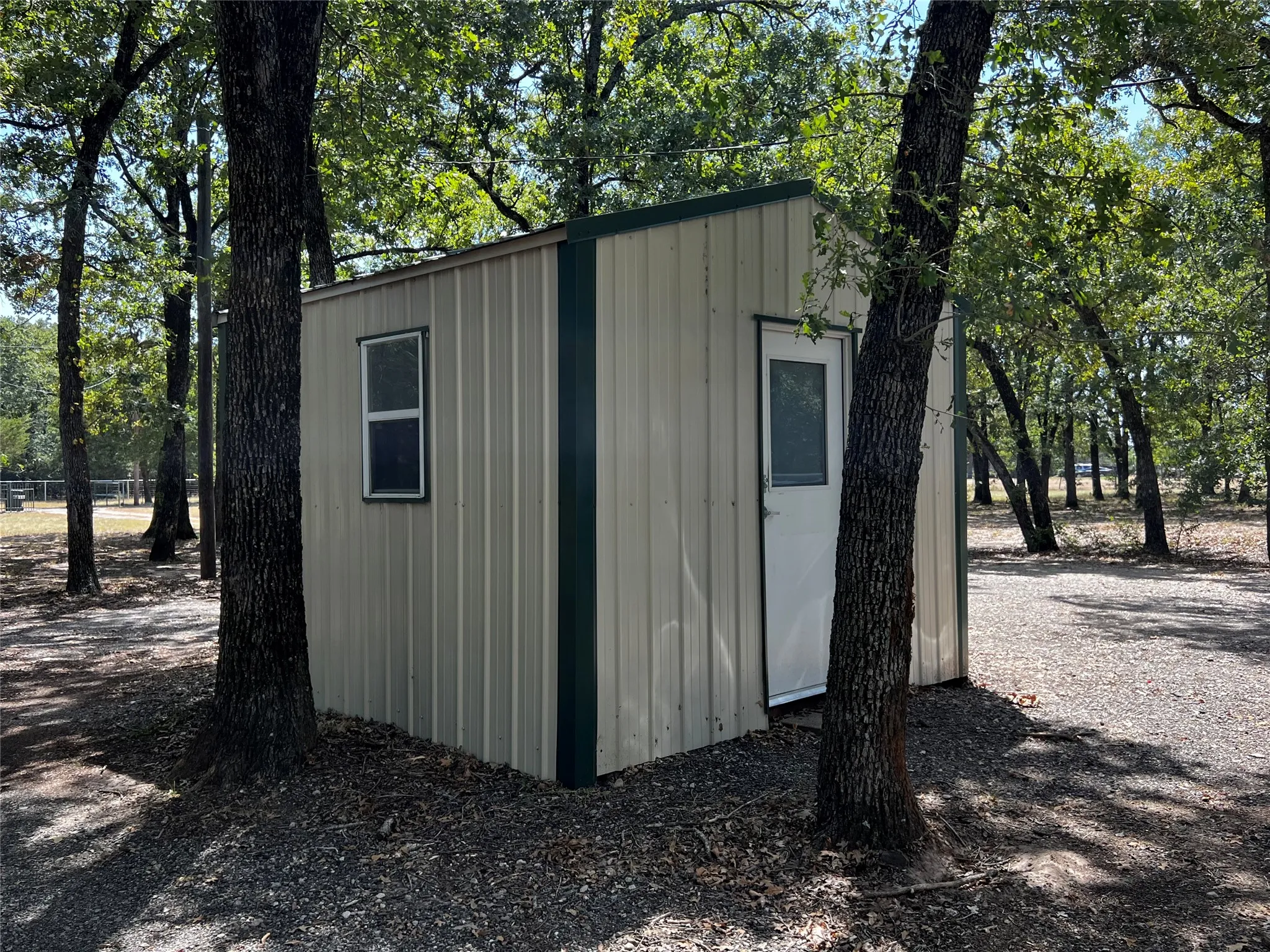 Detached utility shed with a metal exterior, a white entry door, and a green trim roof conveys with the proerty.
