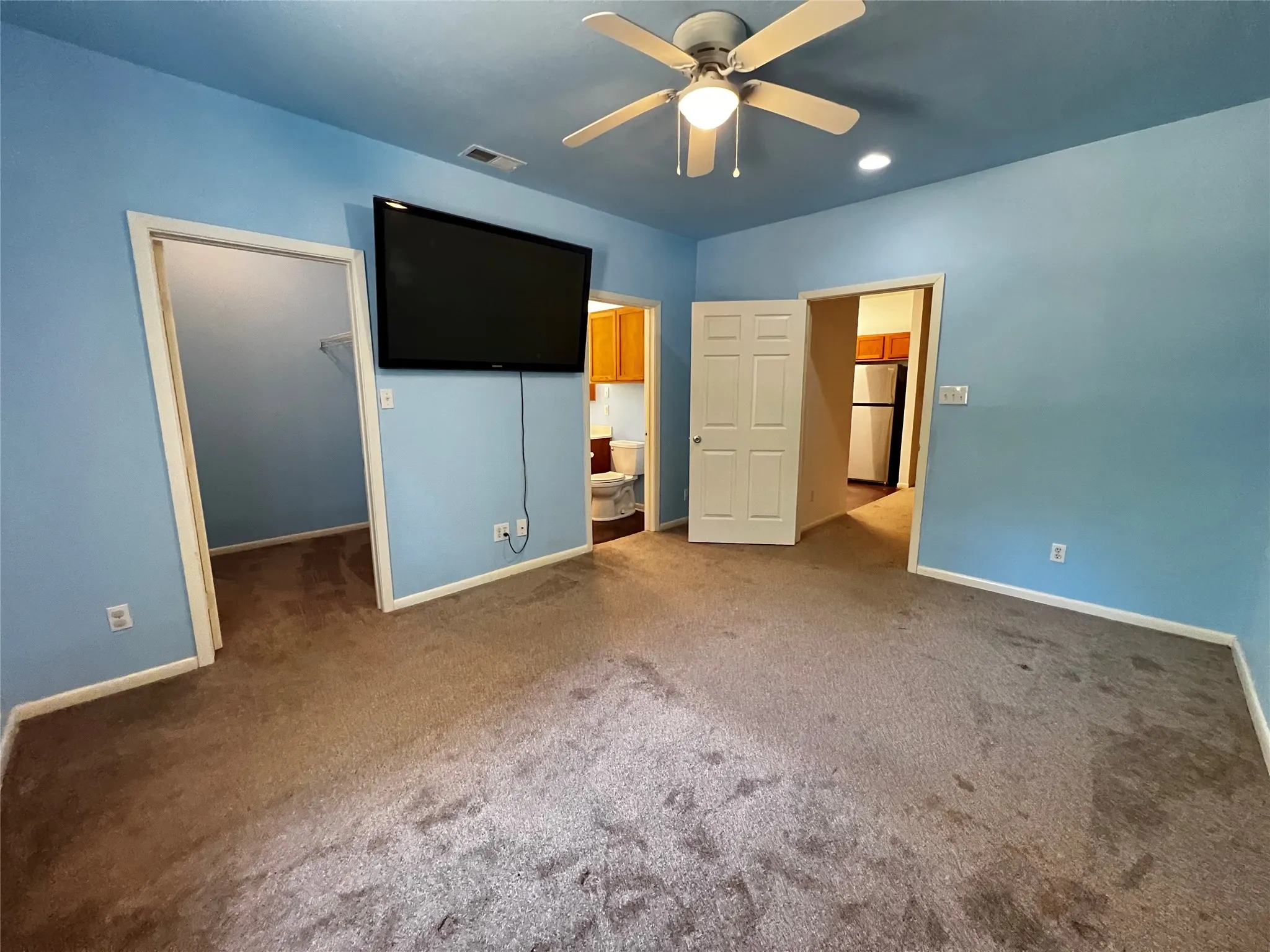 Bedroom #1 showing the walk-in closet and bathroom entrances, door to living are, recessed lighting, and wall-mounted television