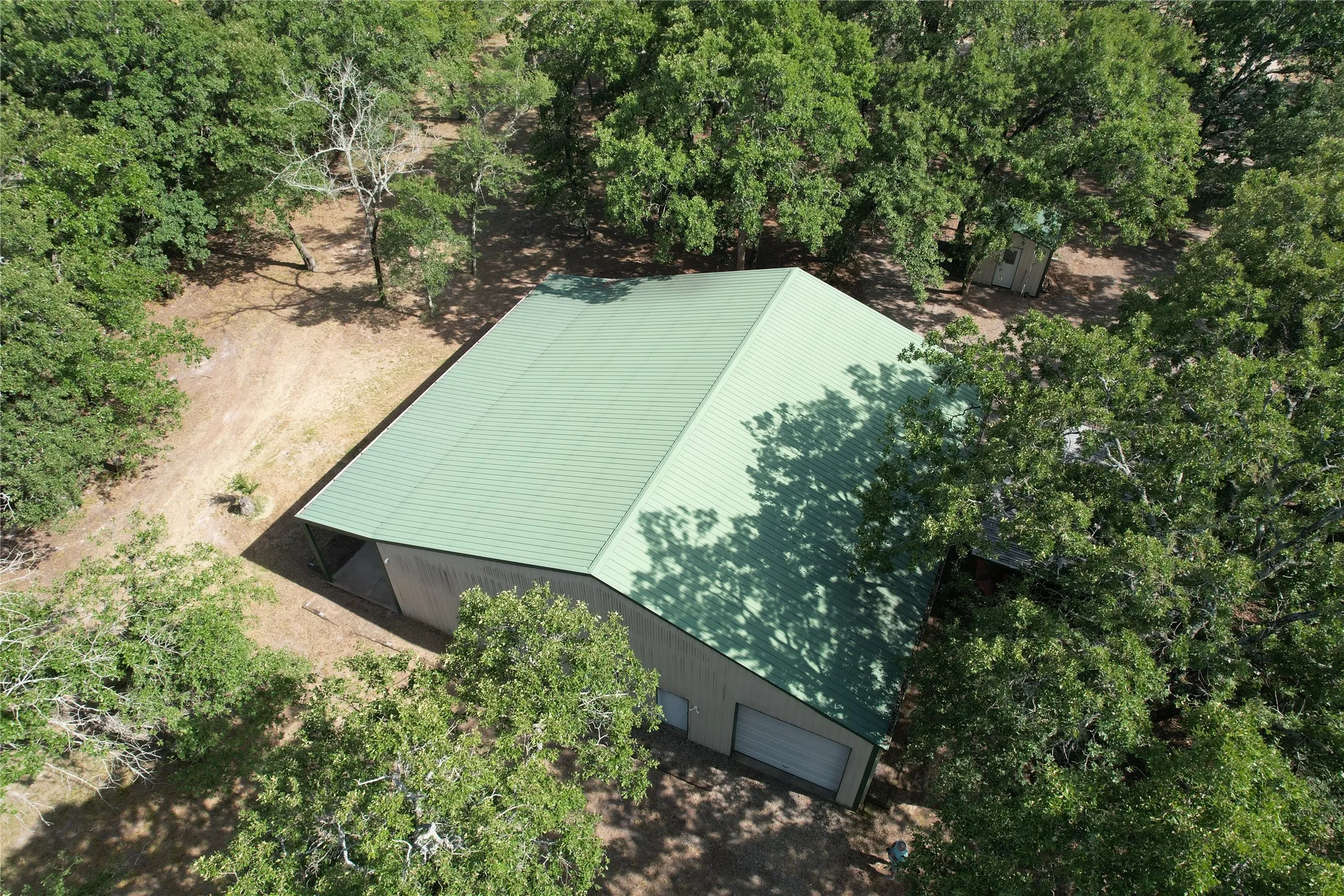Metal building with a green roof, two garage bays, and a side entrance, surrounded by mature trees