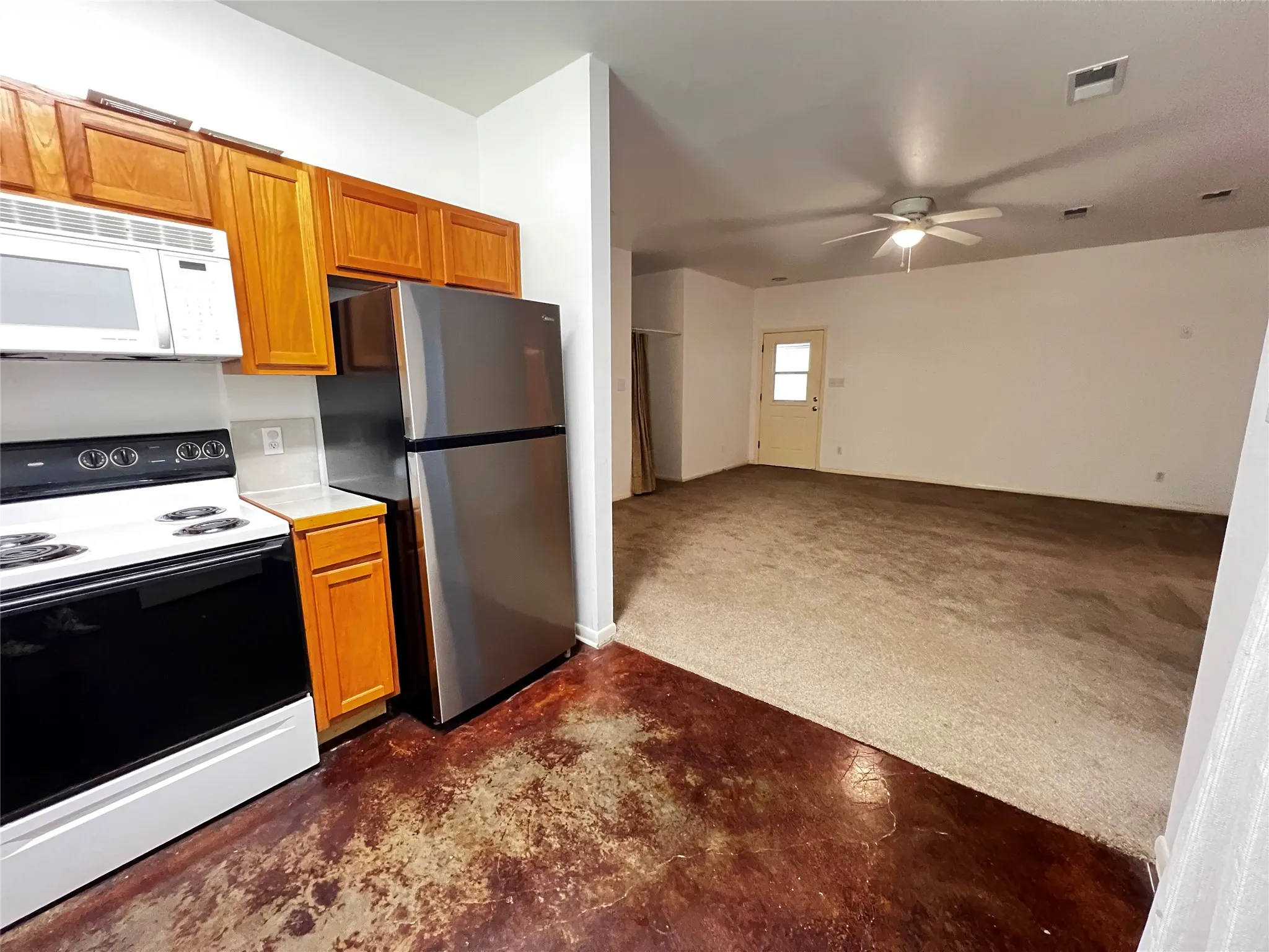 Kitchen with wood-finish cabinetry, stainless steel refrigerator, white microwave,