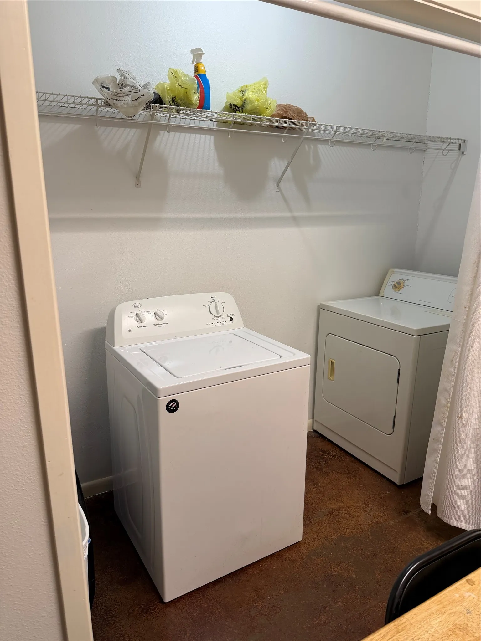 Dedicated utility space featuring a wire shelving unit, brown concrete flooring, and white walls.  Spacious is flexible as a utility - pantry closet.
