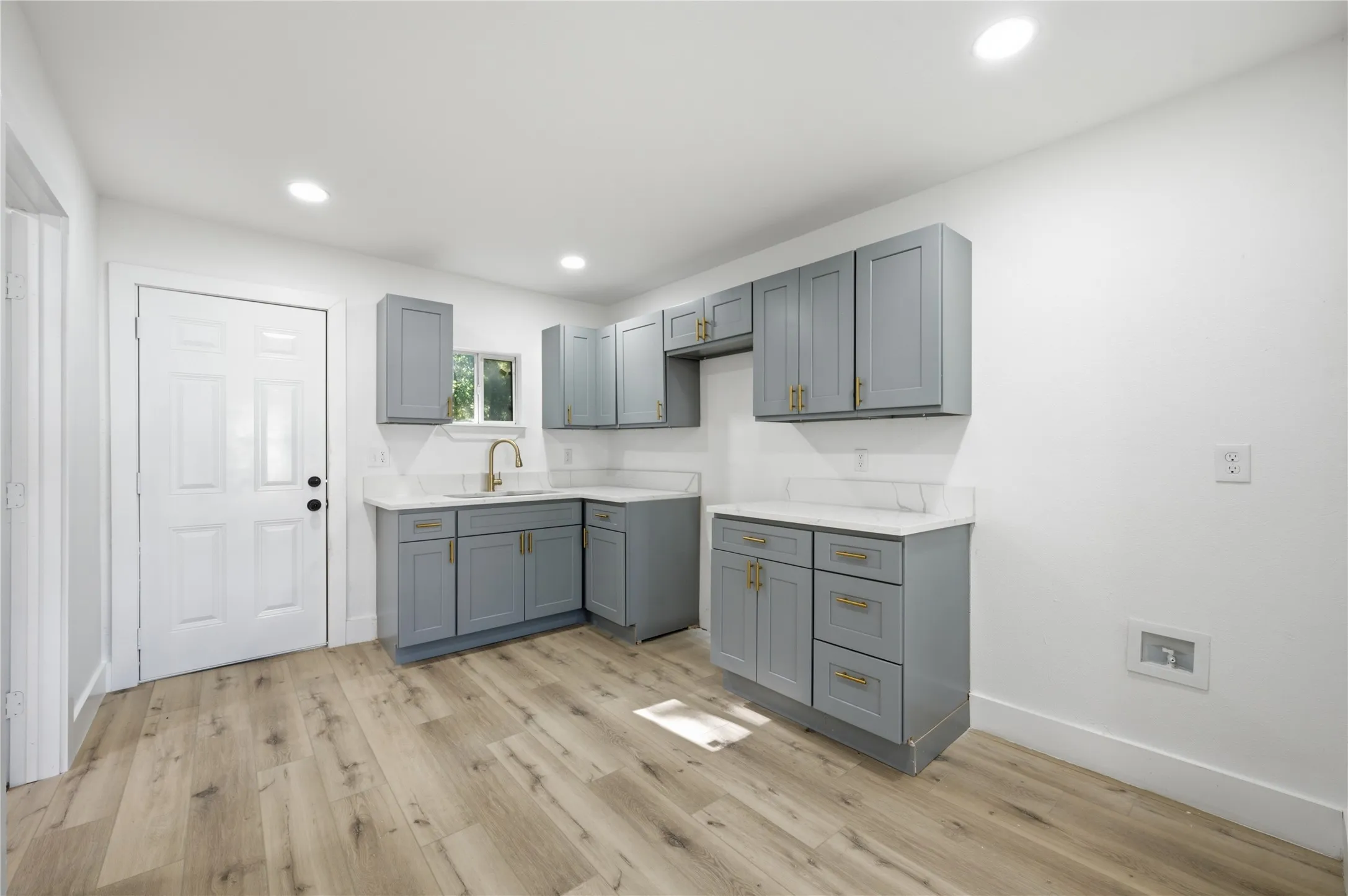 Kitchen featuring light wood-finish flooring, recessed lighting, white walls, gray cabinetry with gold-tone hardware, and white countertops