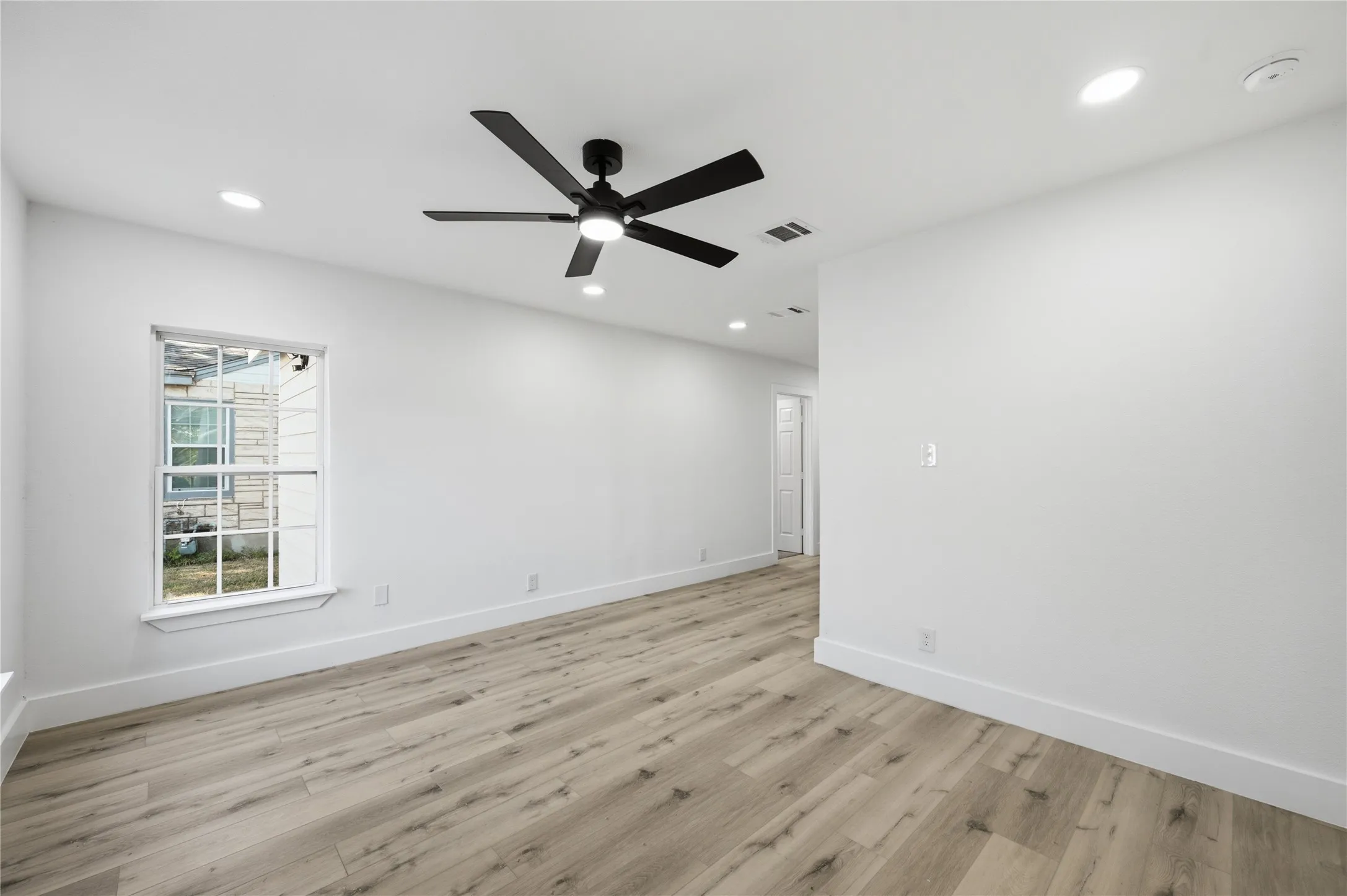 Spacious room featuring light wood-finish flooring, recessed lighting, and a modern black ceiling fan
