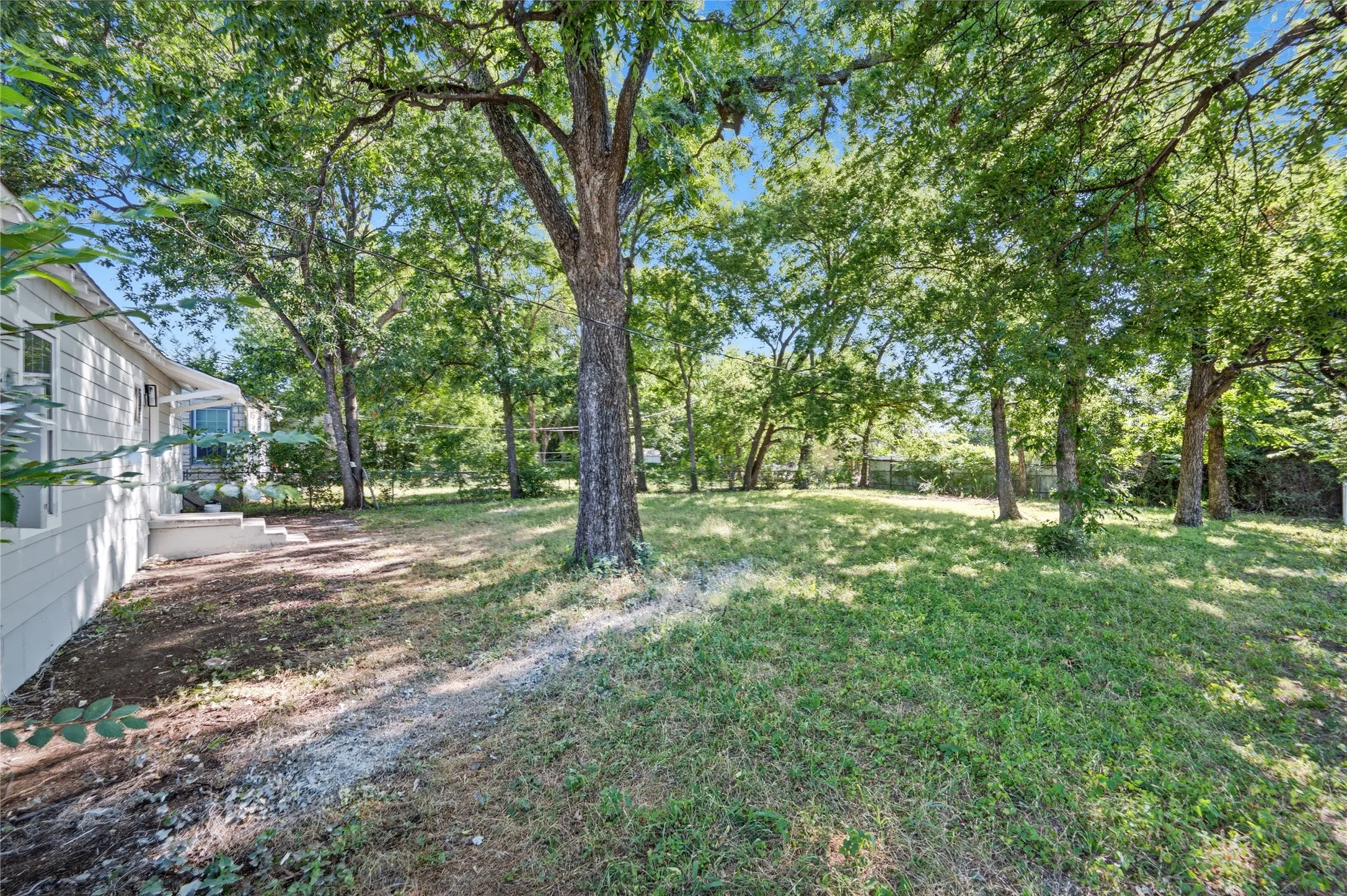 Expansive backyard featuring mature trees, a gently sloping lawn, and a partial privacy fence