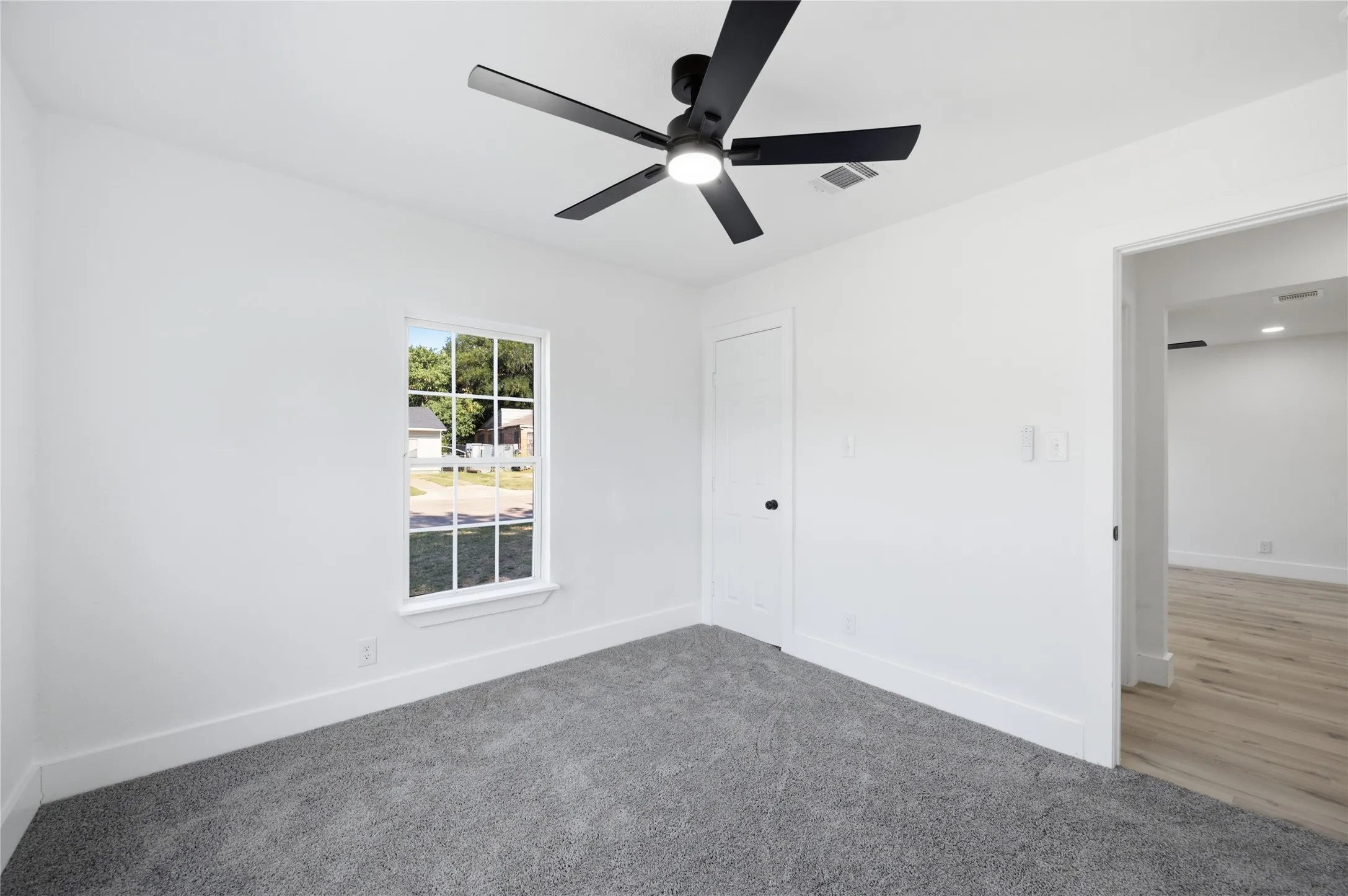 Room featuring gray carpet flooring, white walls, and a black ceiling fan with integrated lighting