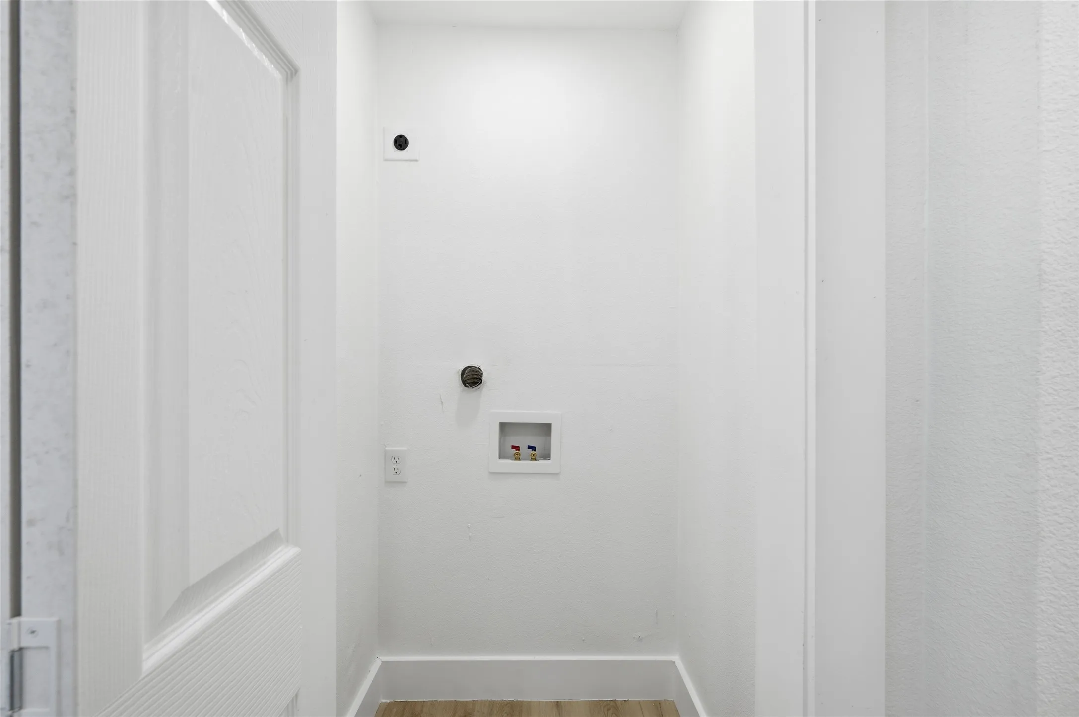 Dedicated utility alcove with pre-plumbed connections for laundry appliances, featuring wood-finish flooring and crisp white walls