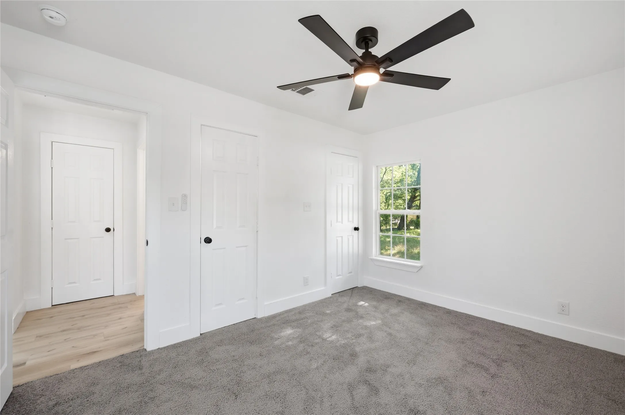 Room featuring gray carpet flooring, white walls, and a black ceiling fan with integrated lighting