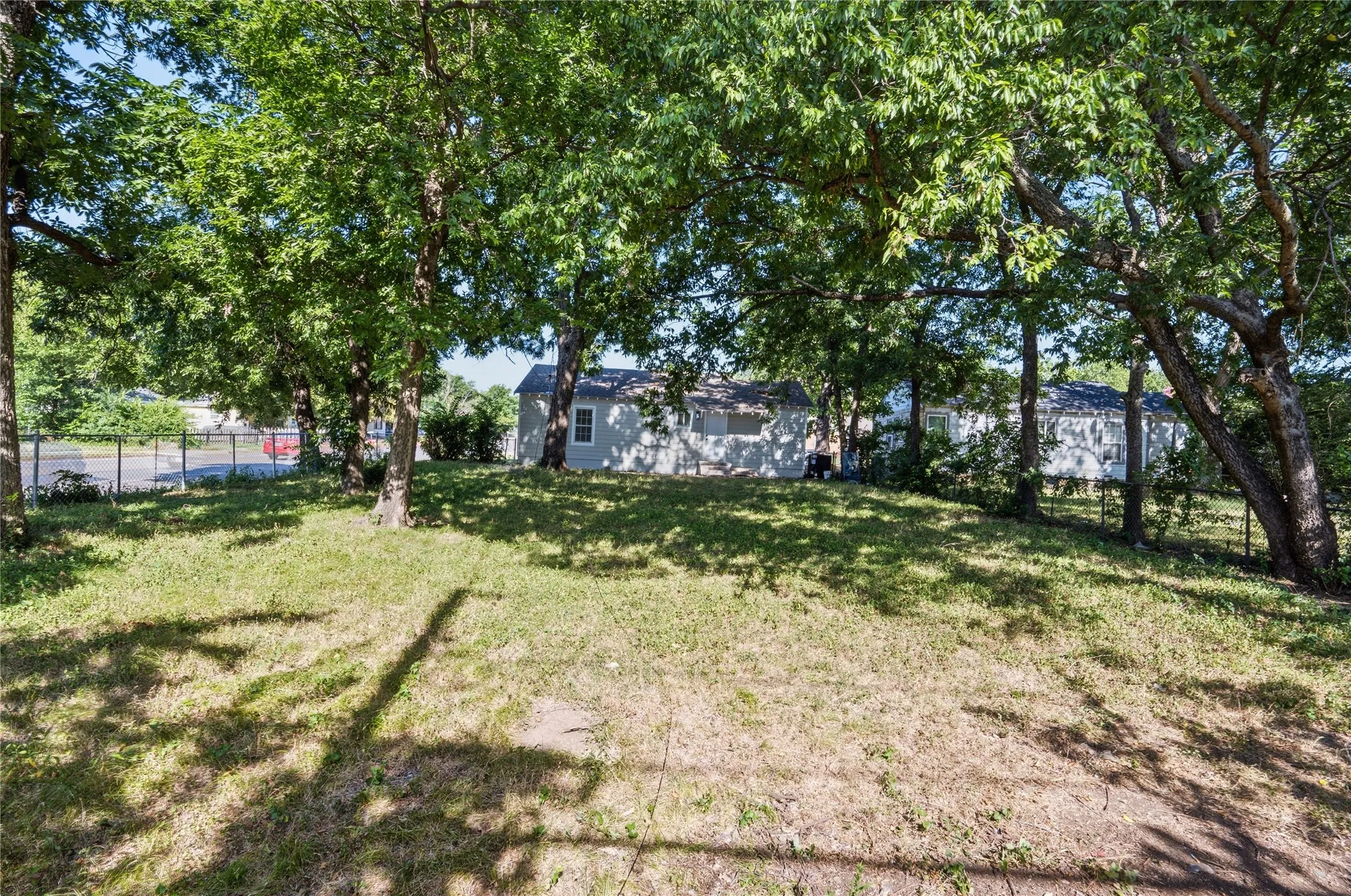 Expansive outdoor space featuring mature trees, partial fencing, and a graded lawn
