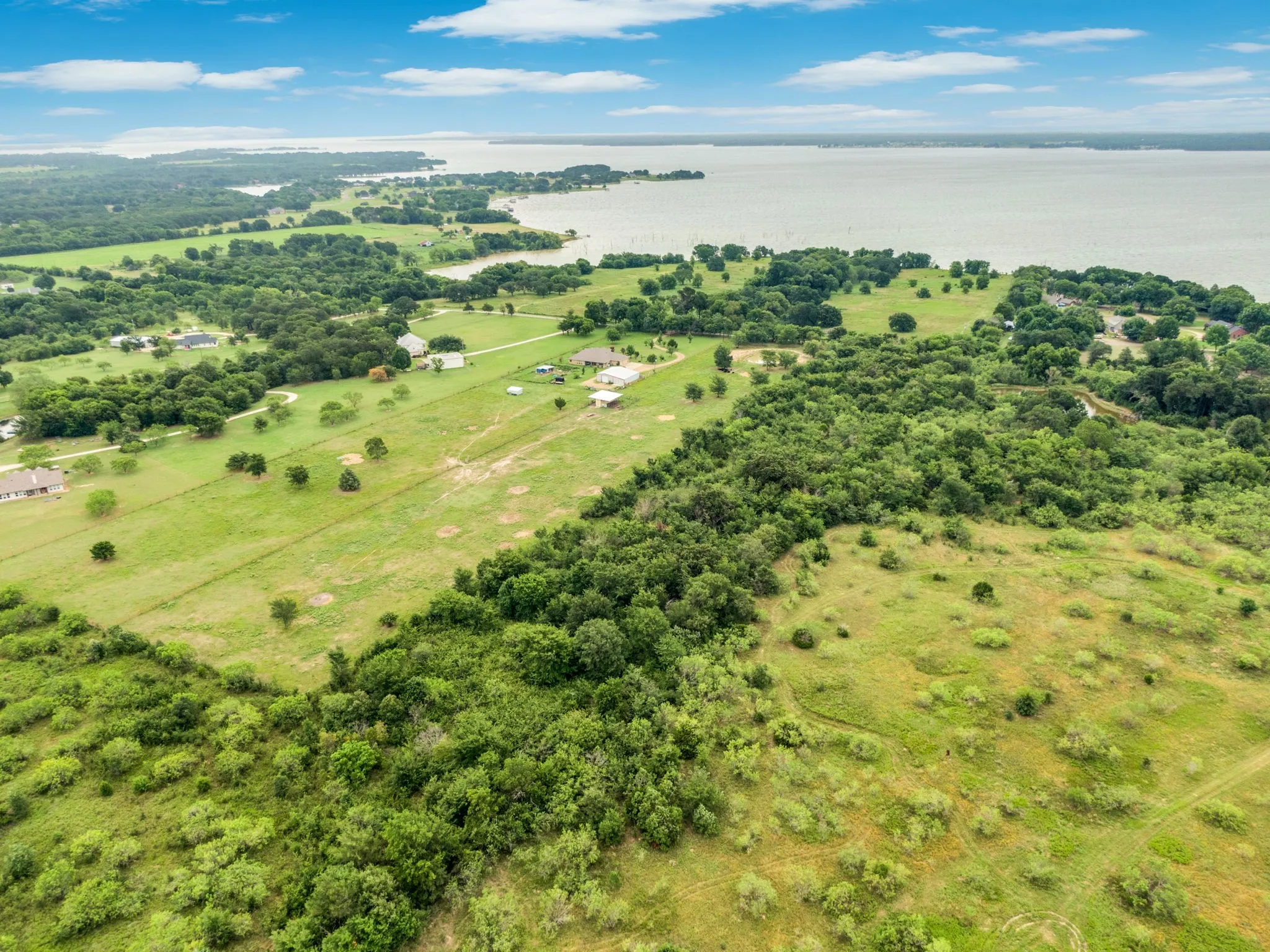 Expansive land parcel featuring a natural tree line, open grassy areas, and a visible body of water in the background