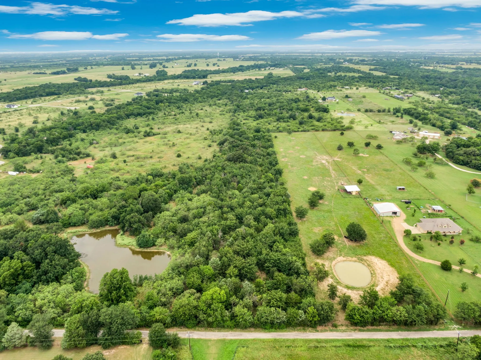 Expansive rural landscape featuring a large wooded area, open fields, and two distinct ponds