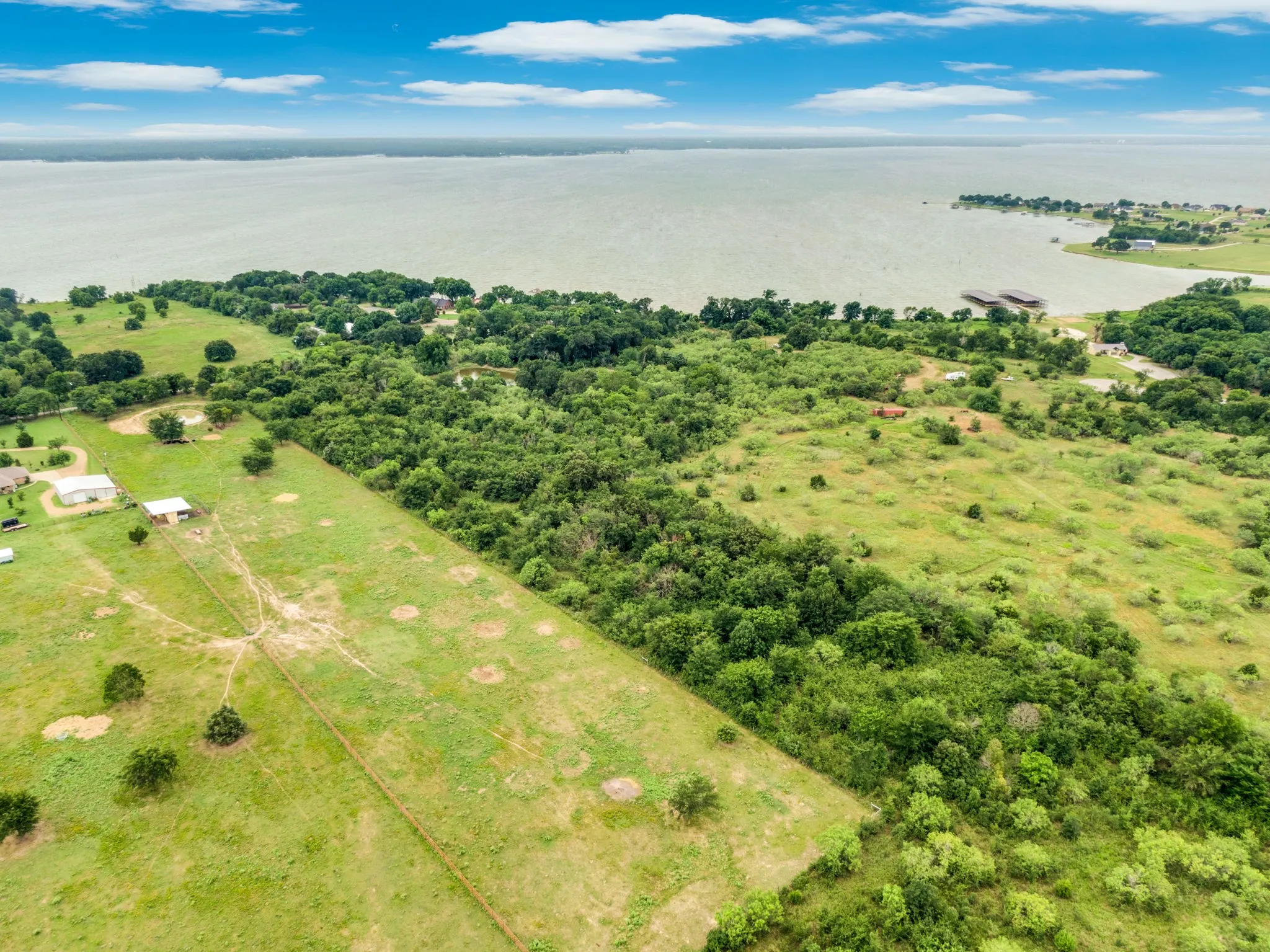 Expansive waterfront property featuring a large body of water, lush green landscape, mature trees, and visible clearings