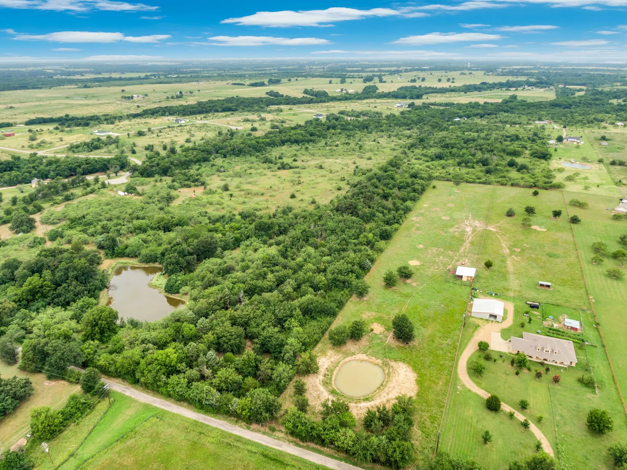 Expansive rural property featuring a large residence, multiple outbuildings, two ponds, and mature tree lines