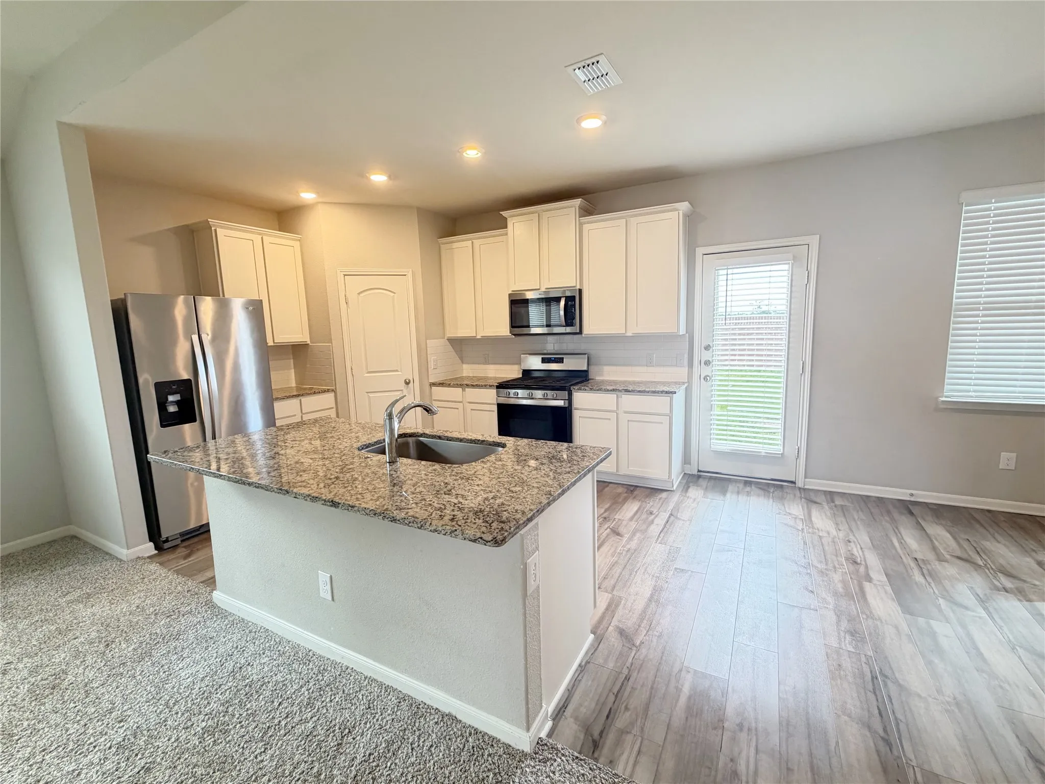 Kitchen featuring a central island with an undermount sink, granite countertop, and stainless steel faucet
