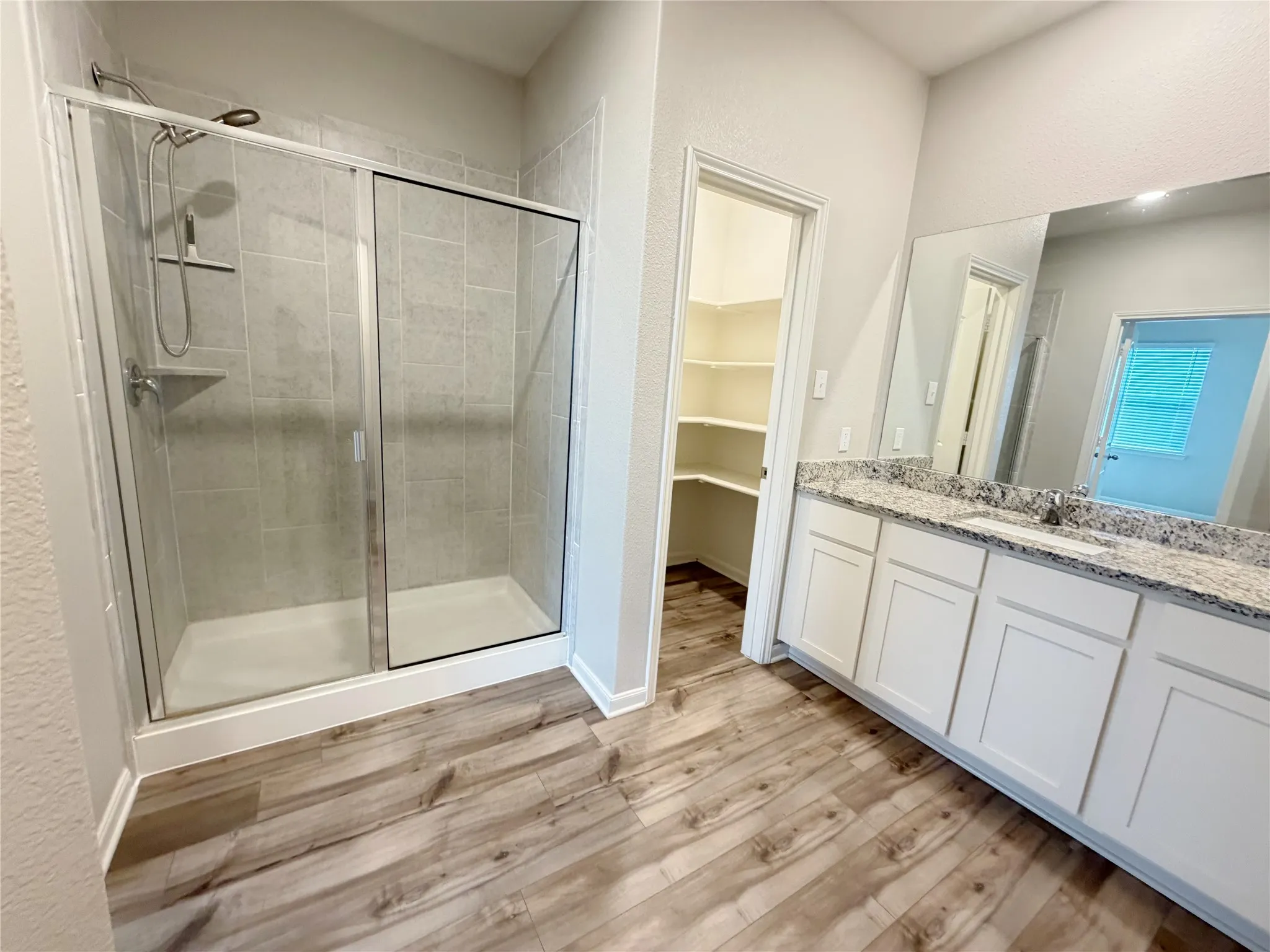 Bathroom featuring a framed glass shower enclosure, tiled shower surround, wood-finish flooring, white vanity cabinetry, and a granite-style countertop with an integrated sink