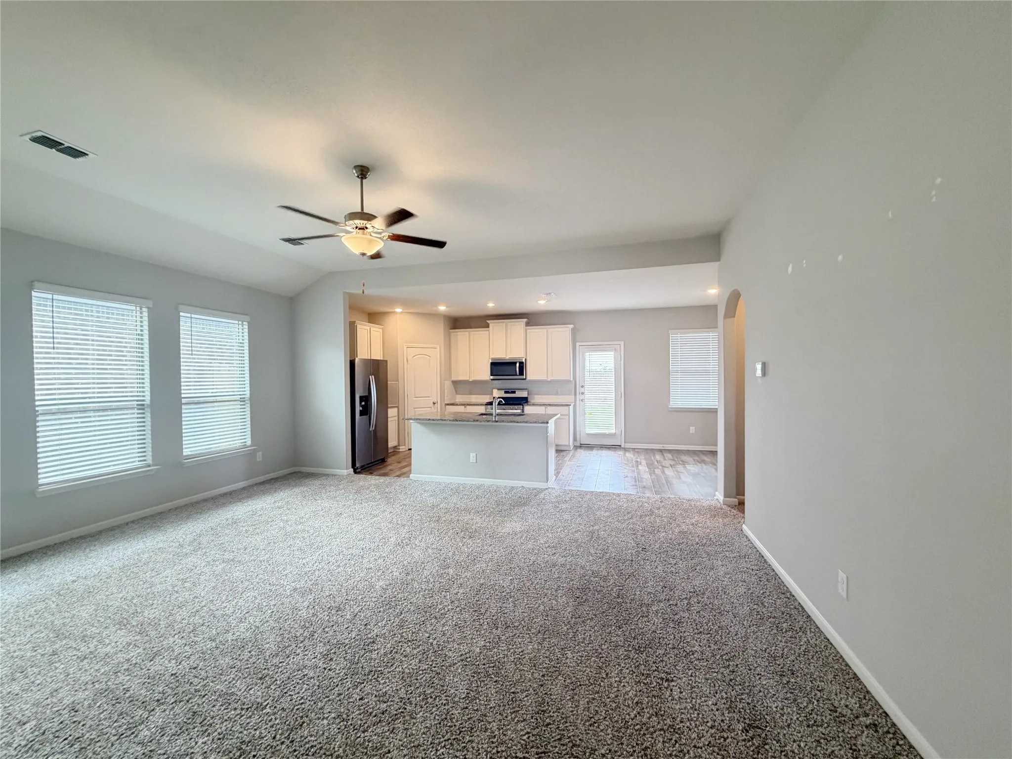 Open-concept living space featuring light gray walls, plush carpet, and a ceiling fan