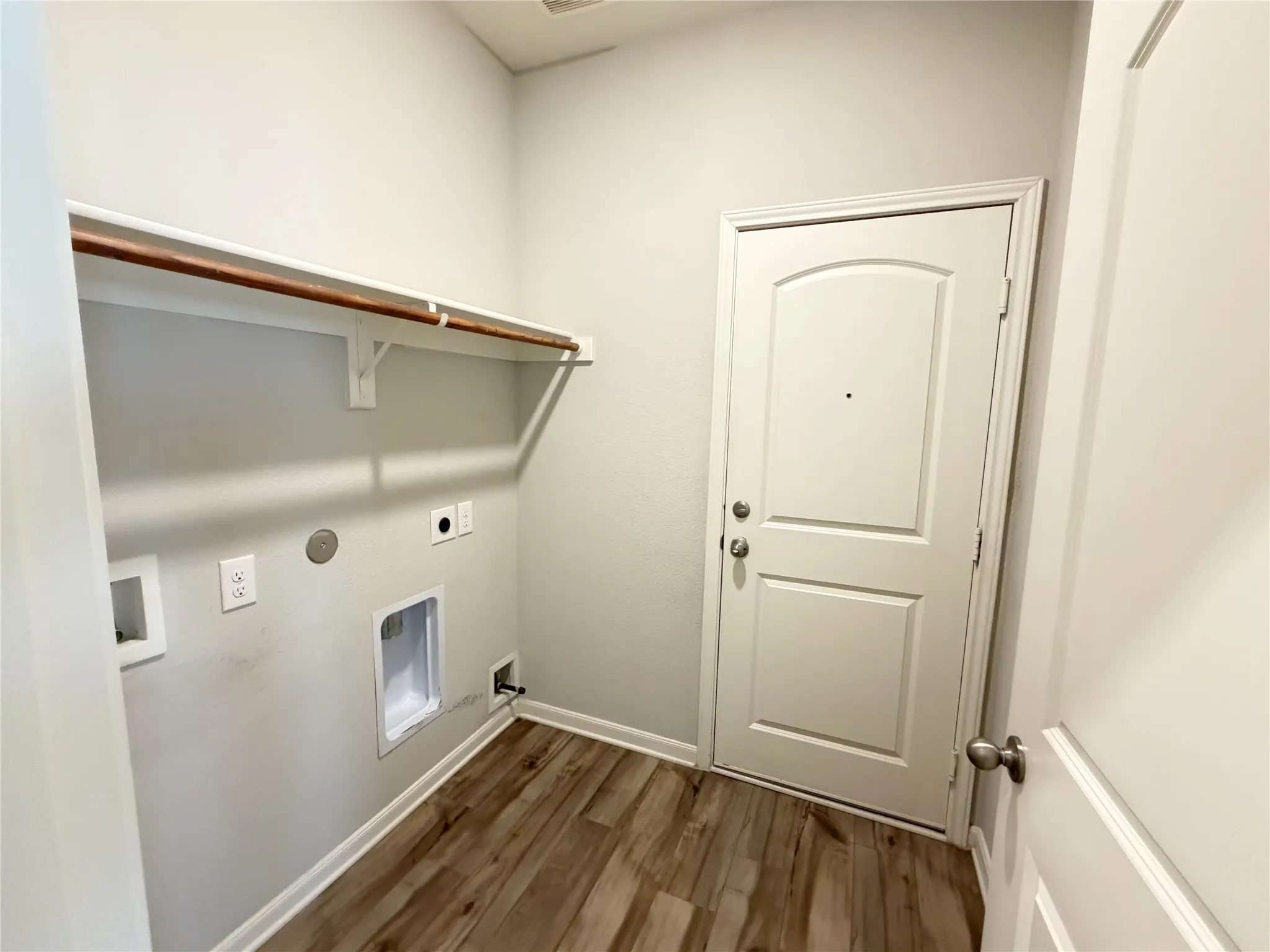 Dedicated laundry area featuring wood-finish flooring, a white paneled door, and a built-in shelving unit with a hanging rod