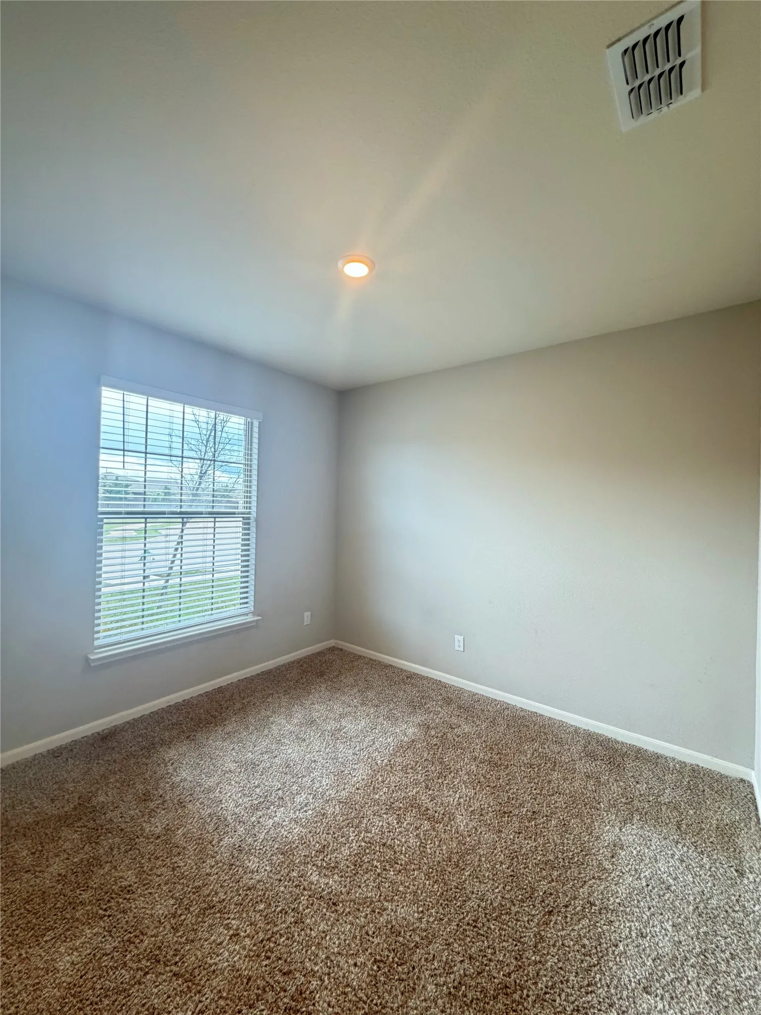 Carpeted room featuring a single window with blinds, a recessed ceiling light, and a ceiling vent
