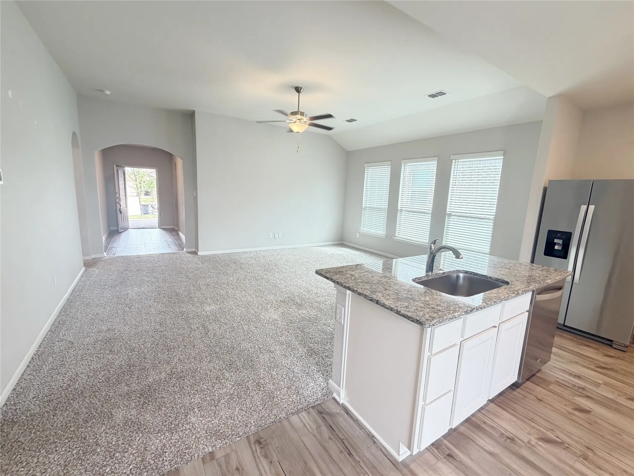 Open-concept living space featuring a kitchen island with granite countertops, stainless steel sink, and white cabinetry