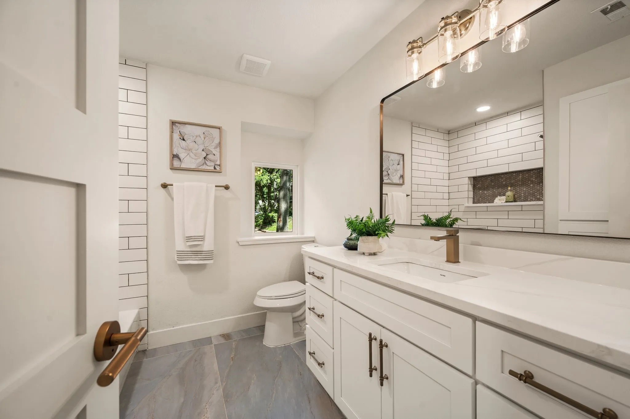 The secondary bath combines a long quartz vanity, abundant storage, modern lighting, and timeless finishes.