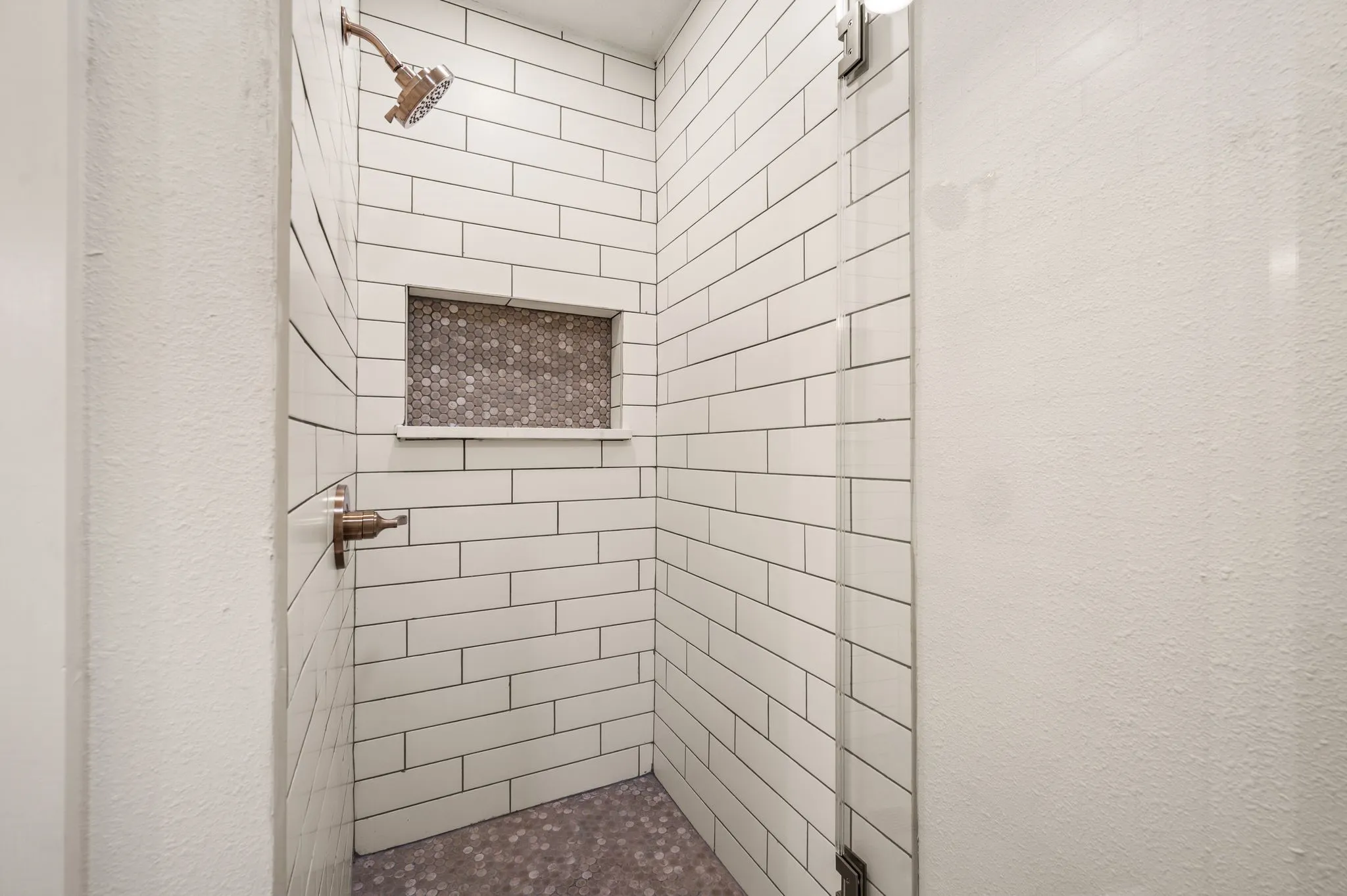Classic white tile, a contrasting mosaic niche, and a glass enclosure create a crisp, timeless shower.