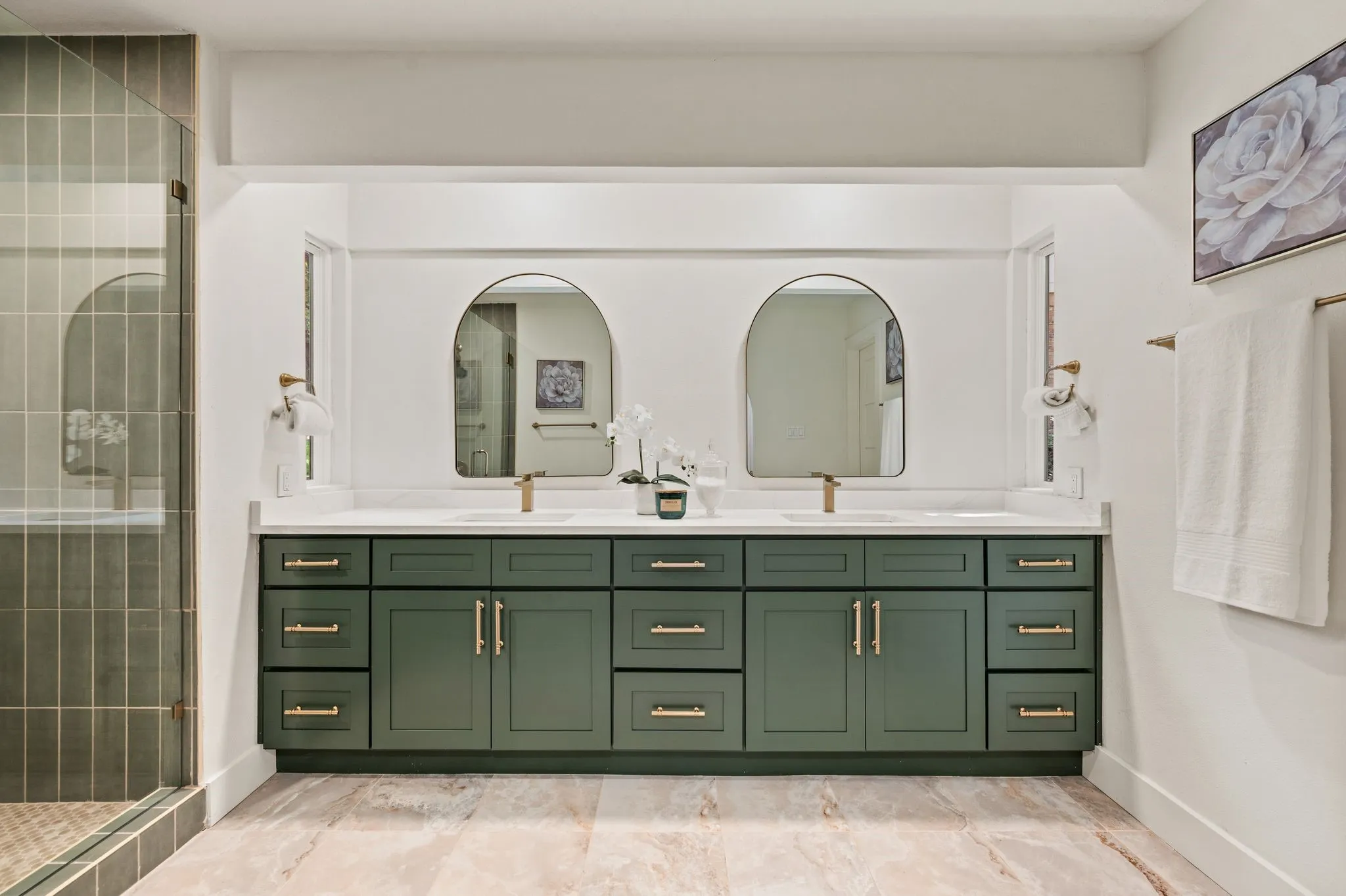 A sage-green double vanity, quartz counters, arched mirrors, and champagne-bronze accents create understated luxury.