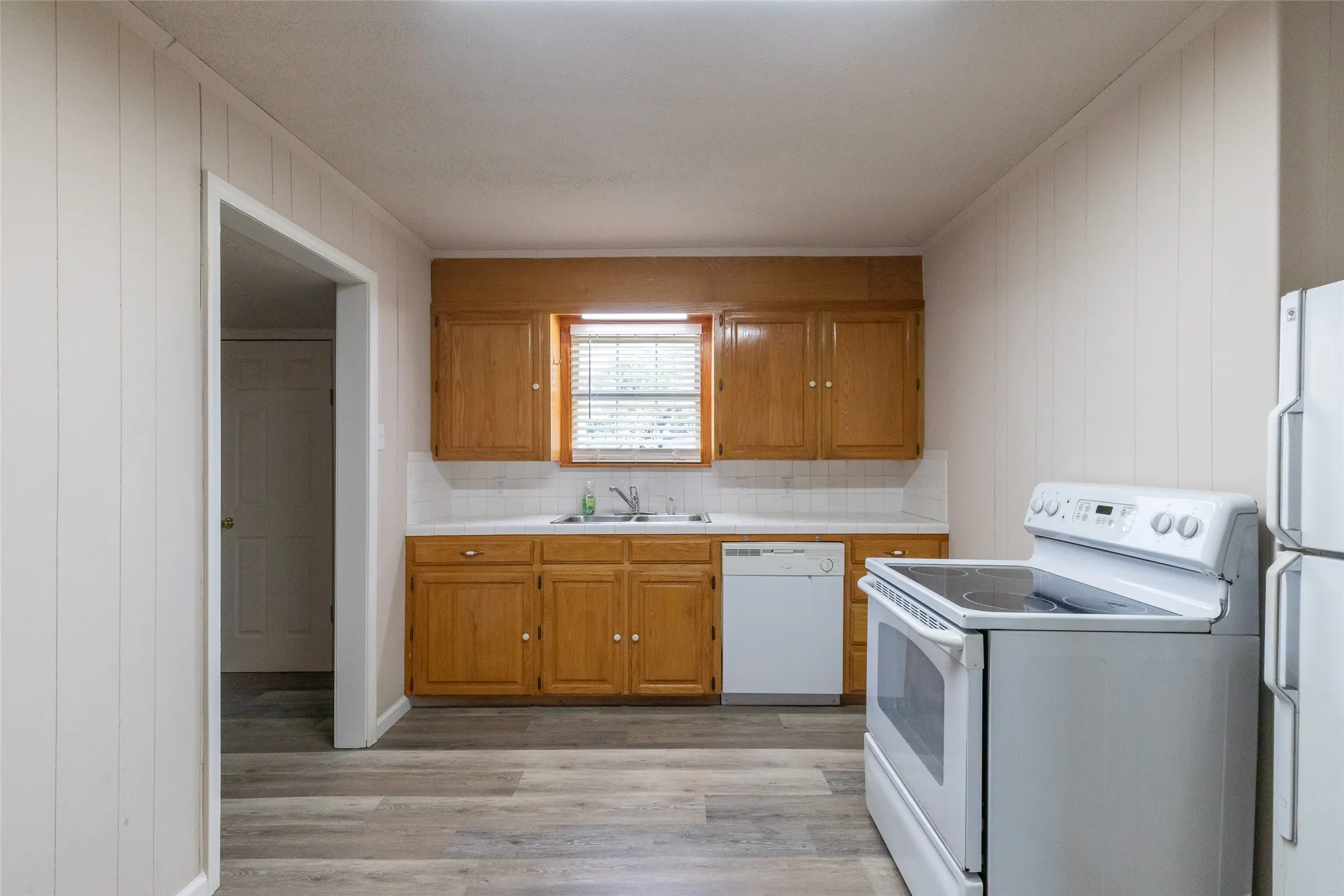 Kitchen featuring wood-finish cabinetry, white countertops, a white tile backsplash, and wood-finish flooring