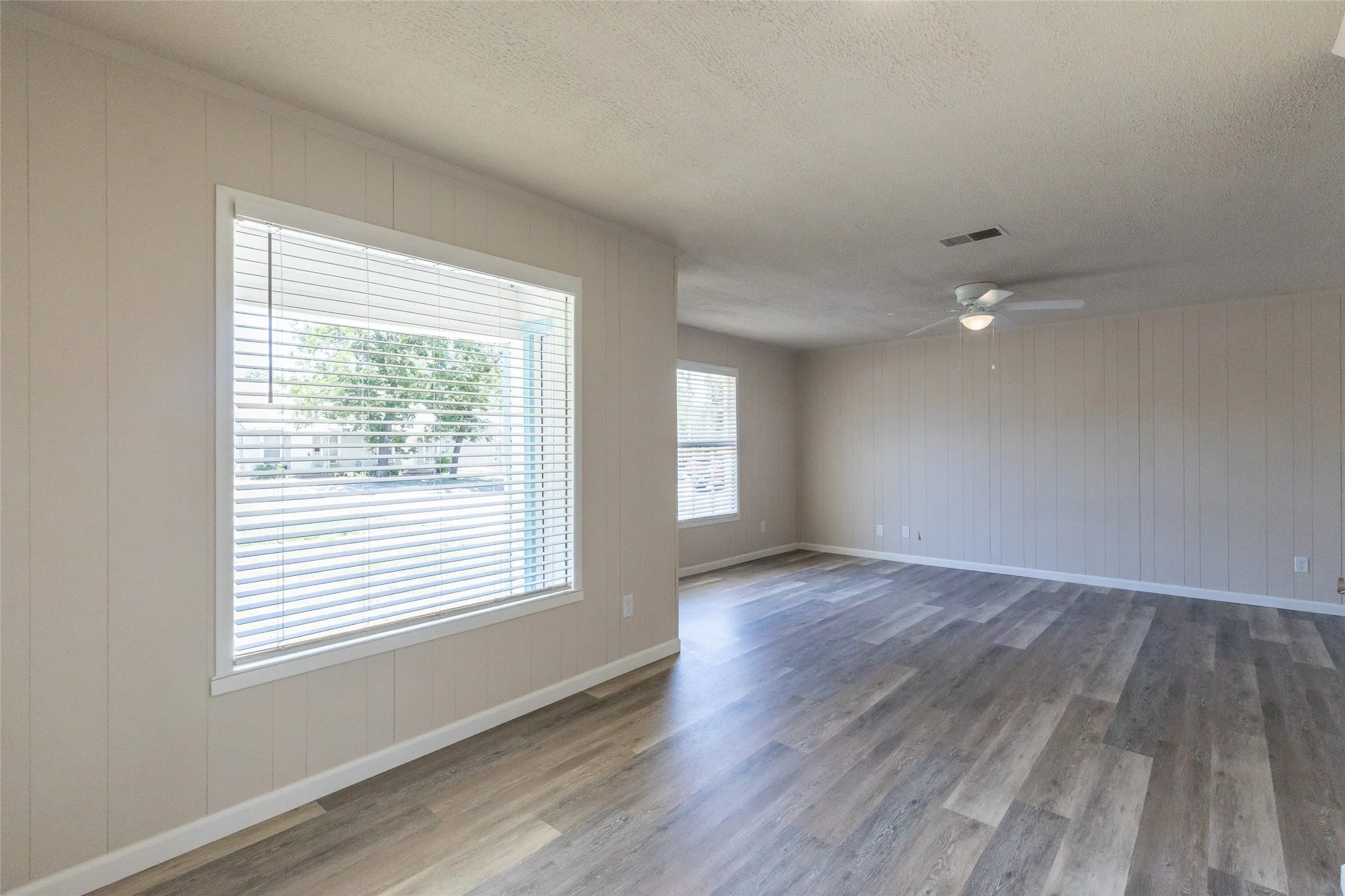 Spacious interior featuring wood-finish flooring, vertical paneling, and a ceiling fan with integrated lighting