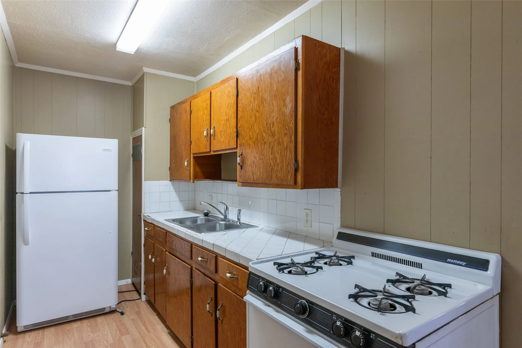 Kitchen featuring wood-finish cabinetry, white tile countertops, a double basin stainless steel sink, and a white freestanding range
