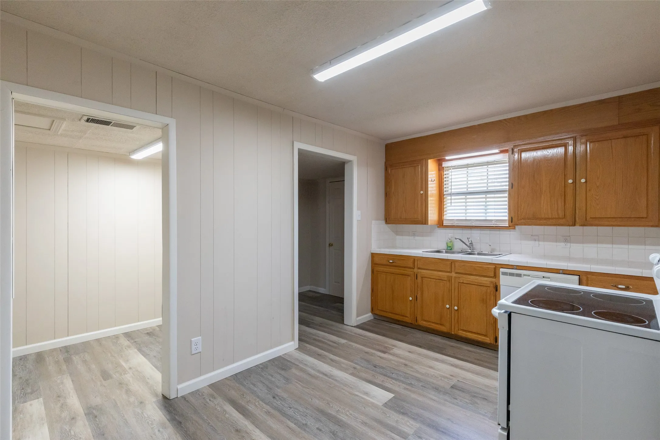 Kitchen featuring wood cabinetry, a white tile backsplash, and a window with horizontal blinds