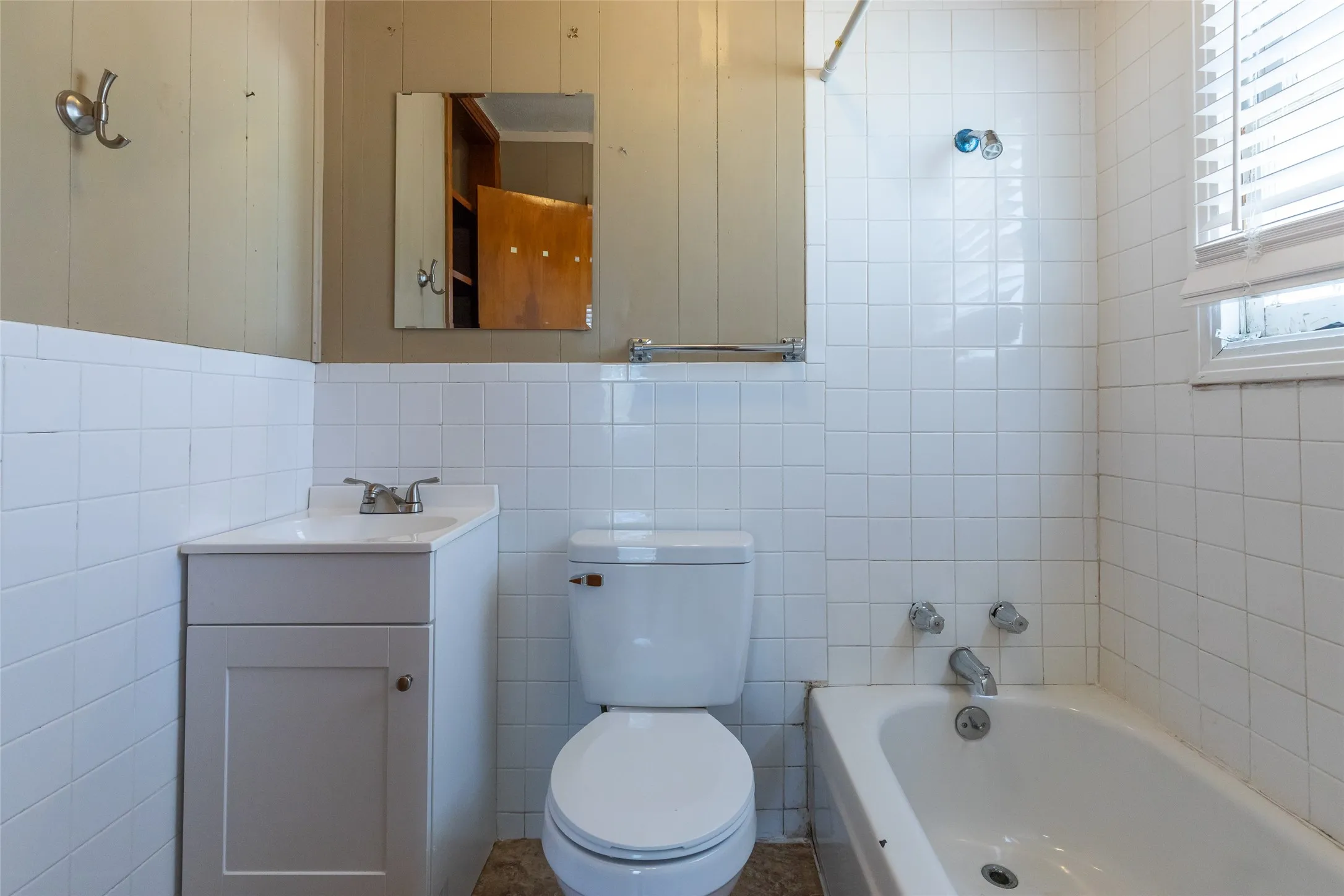 Bathroom featuring white tiled walls, a white vanity with integrated sink, a standard toilet, and a bathtub with chrome fixtures