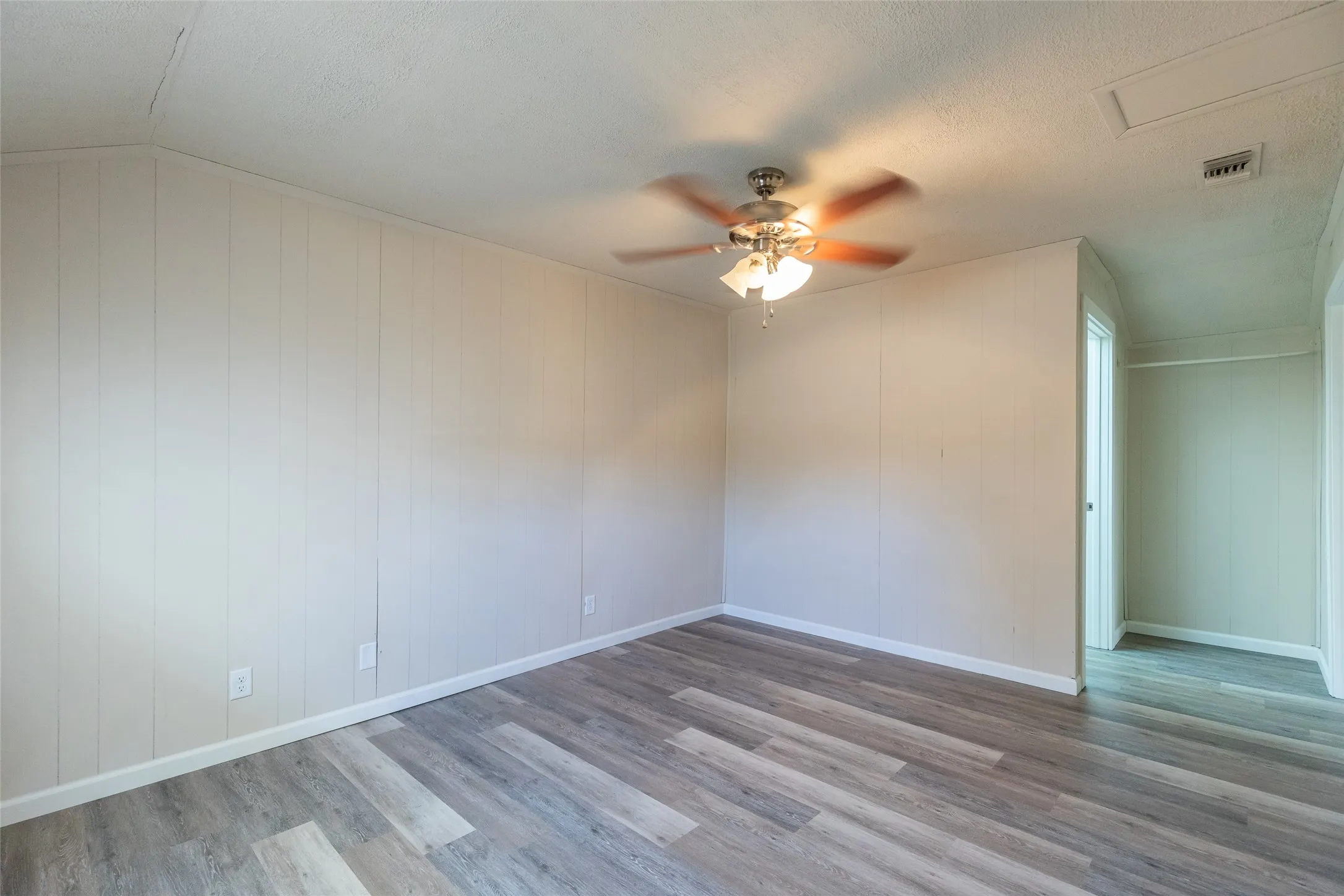 Interior room featuring wood-finish flooring, white panel walls, and a ceiling fan with integrated lighting