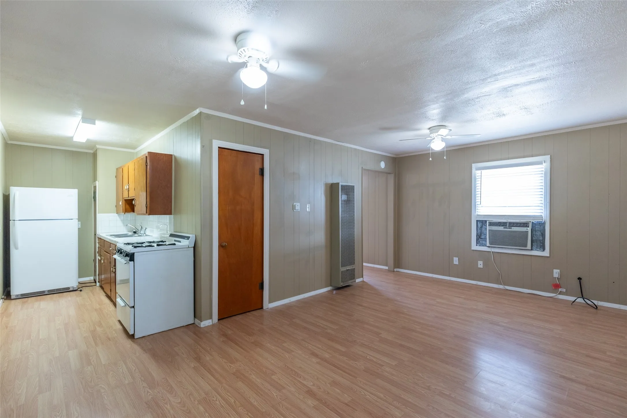Open-concept living space featuring wood-finish flooring, a kitchen area with white appliances, and ceiling fan lighting