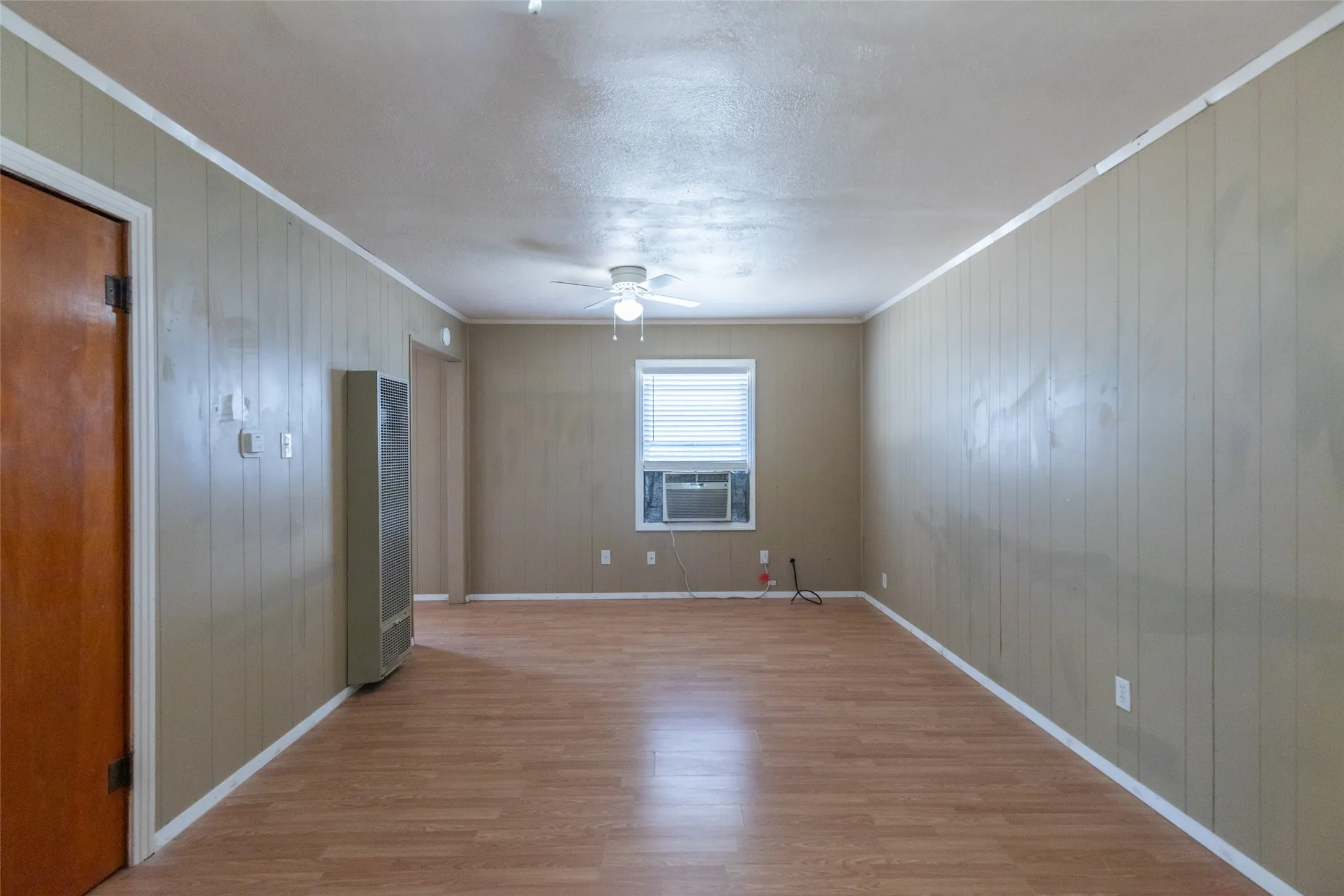 Room featuring wood-finish flooring, vertical paneling, and a ceiling fan with integrated lighting