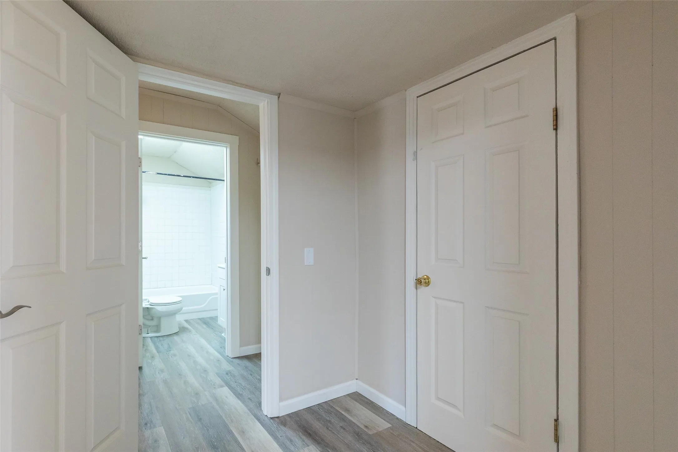 Bathroom entrance featuring a white panel door, wood-finish flooring, and light-toned wall paneling
