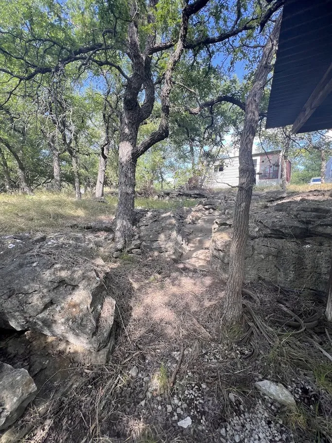 Natural landscape featuring mature trees, exposed rock formations, and a dirt path
