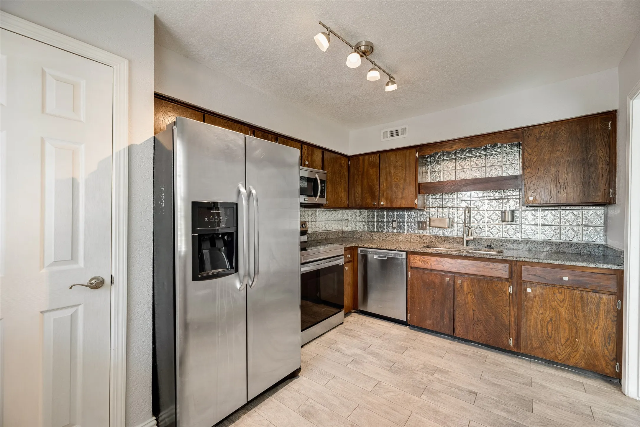 Kitchen featuring wood cabinetry, stainless steel appliances, a patterned backsplash, granite-finish countertops, and light-toned wood-finish flooring