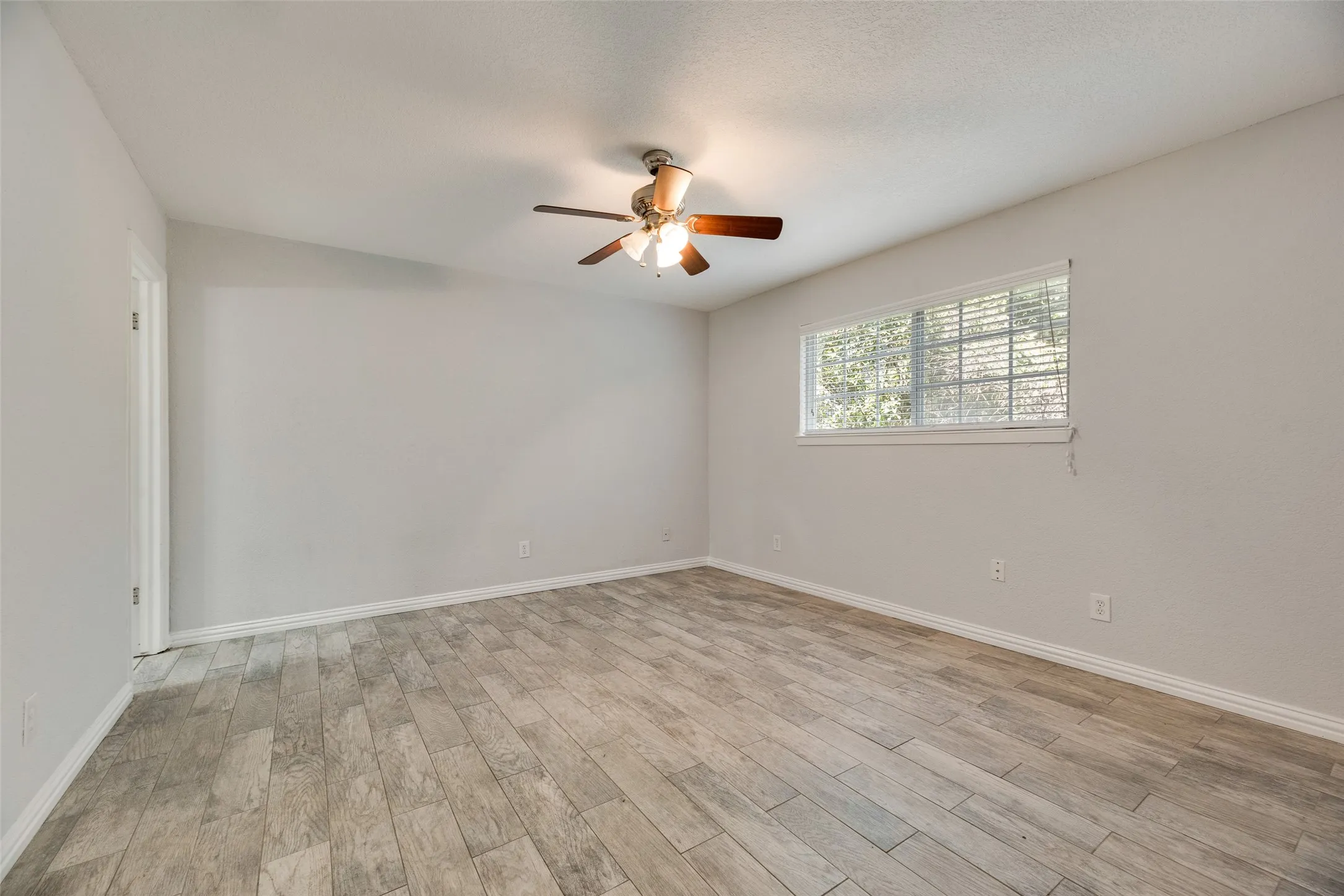 Spacious room featuring wood-finish flooring, light grey wall paint, and a ceiling fan with integrated lighting