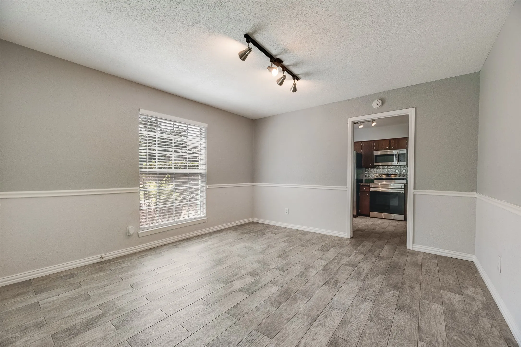 Spacious room featuring wood-finish flooring, two-tone walls with chair rail molding, and a track lighting fixture