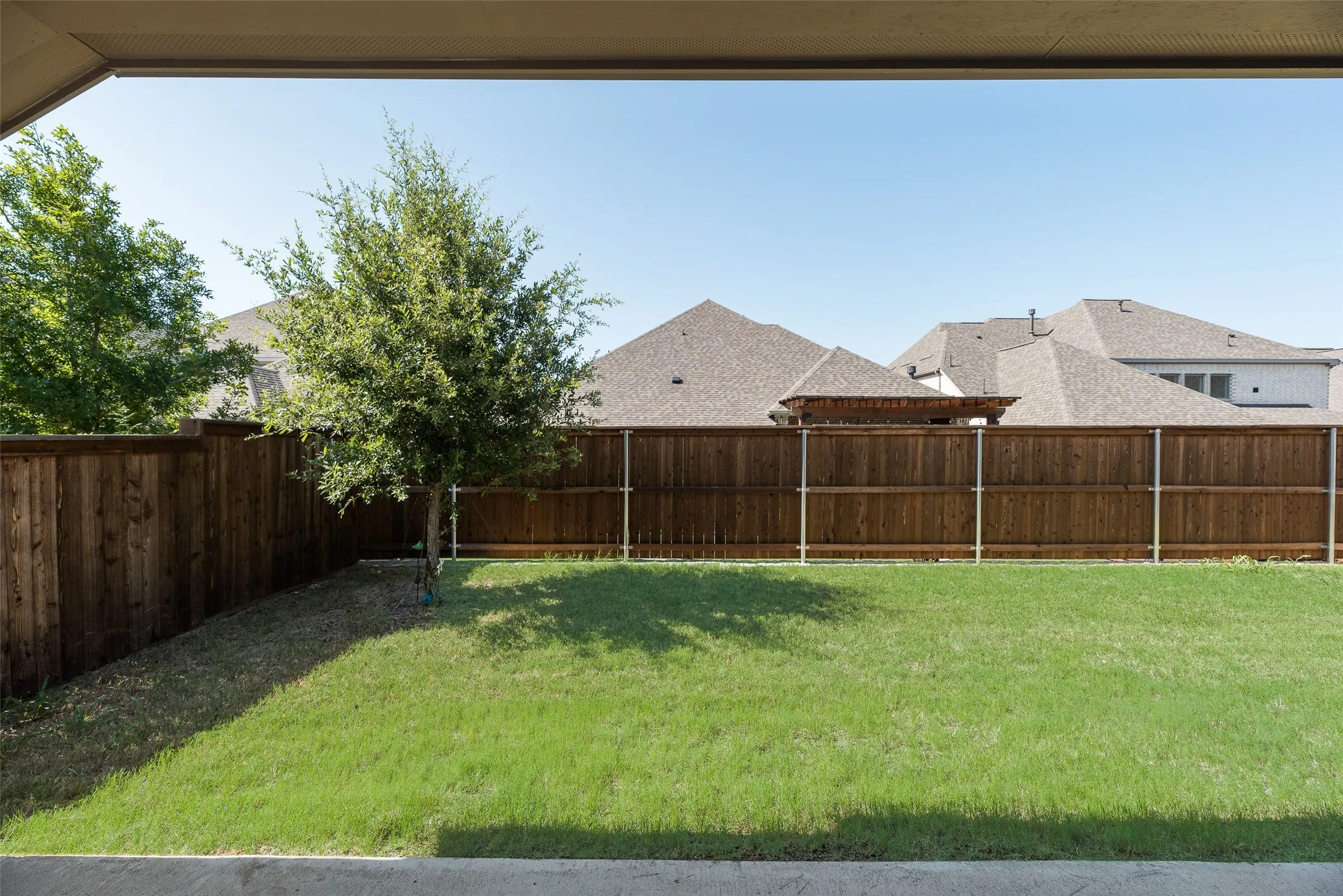 Expansive backyard featuring a lush lawn, mature perimeter tree, and a tall wood privacy fence