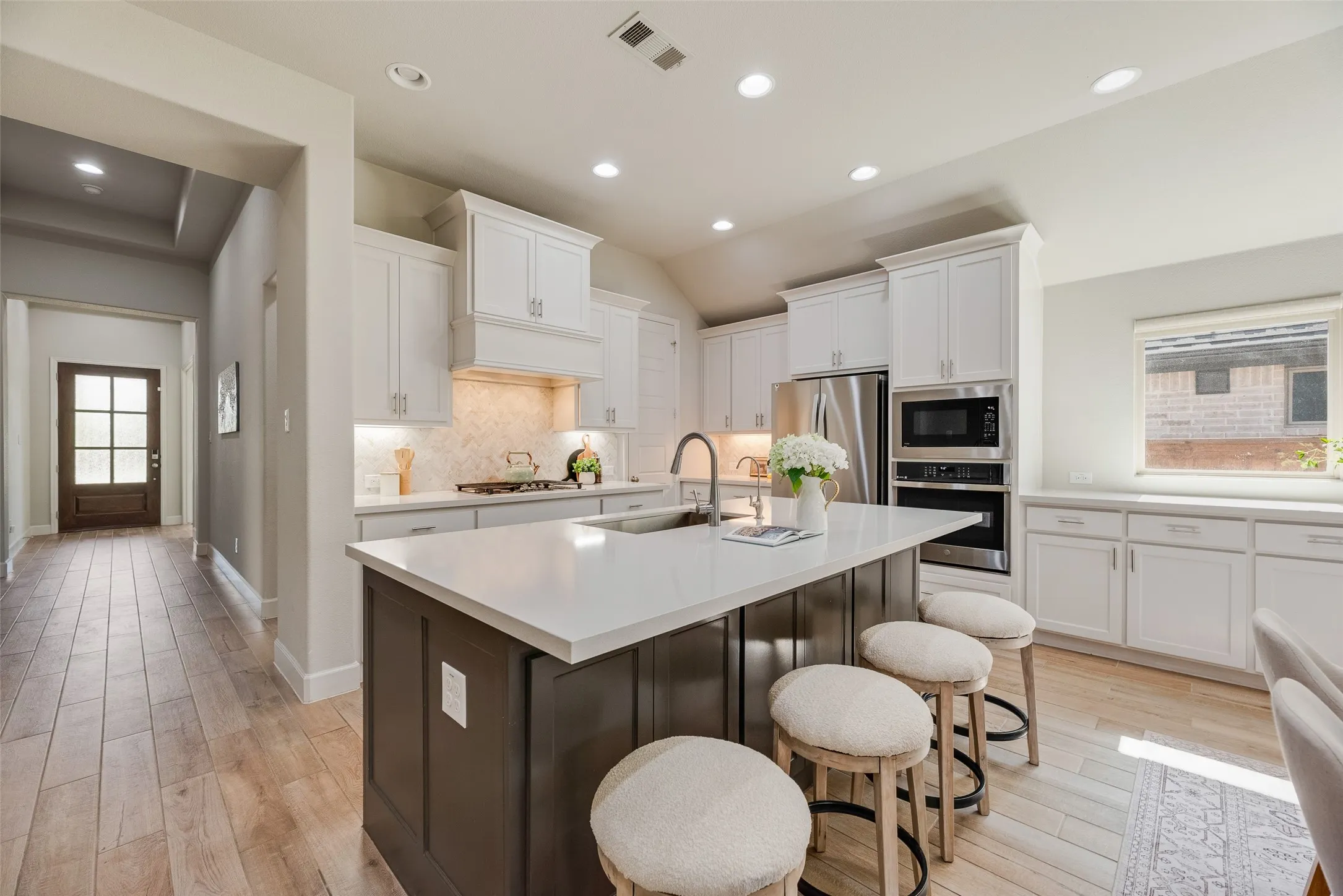 Contemporary kitchen featuring white cabinetry, a built-in stainless steel appliance suite, a large center island with a white countertop, and wood-finish flooring