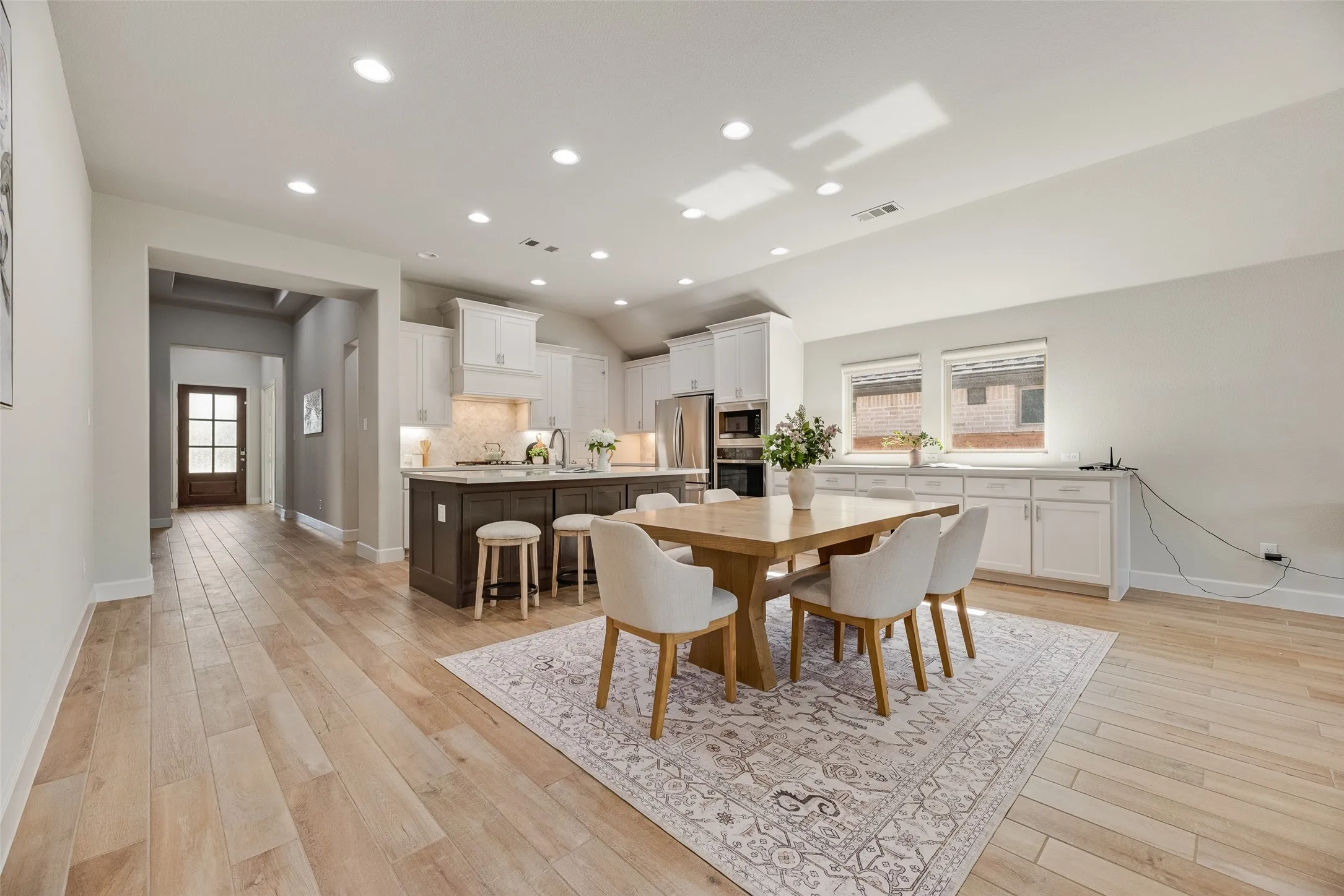 Open-concept living area featuring light wood-finish flooring, recessed lighting, a vaulted ceiling, and a kitchen island with seating