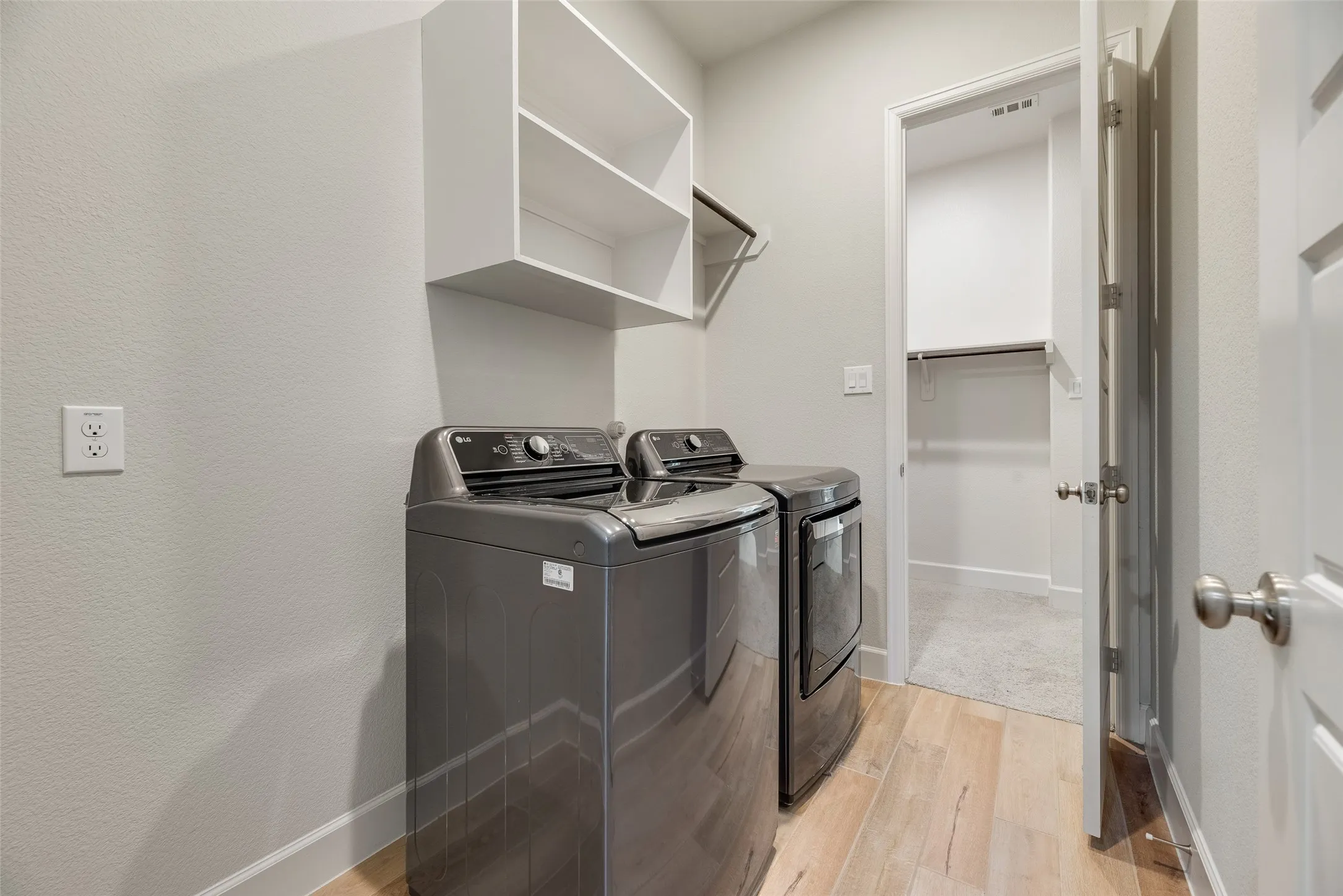 Laundry area featuring wood-finish flooring, white built-in shelving, and a hanging rod has entry to primary closet