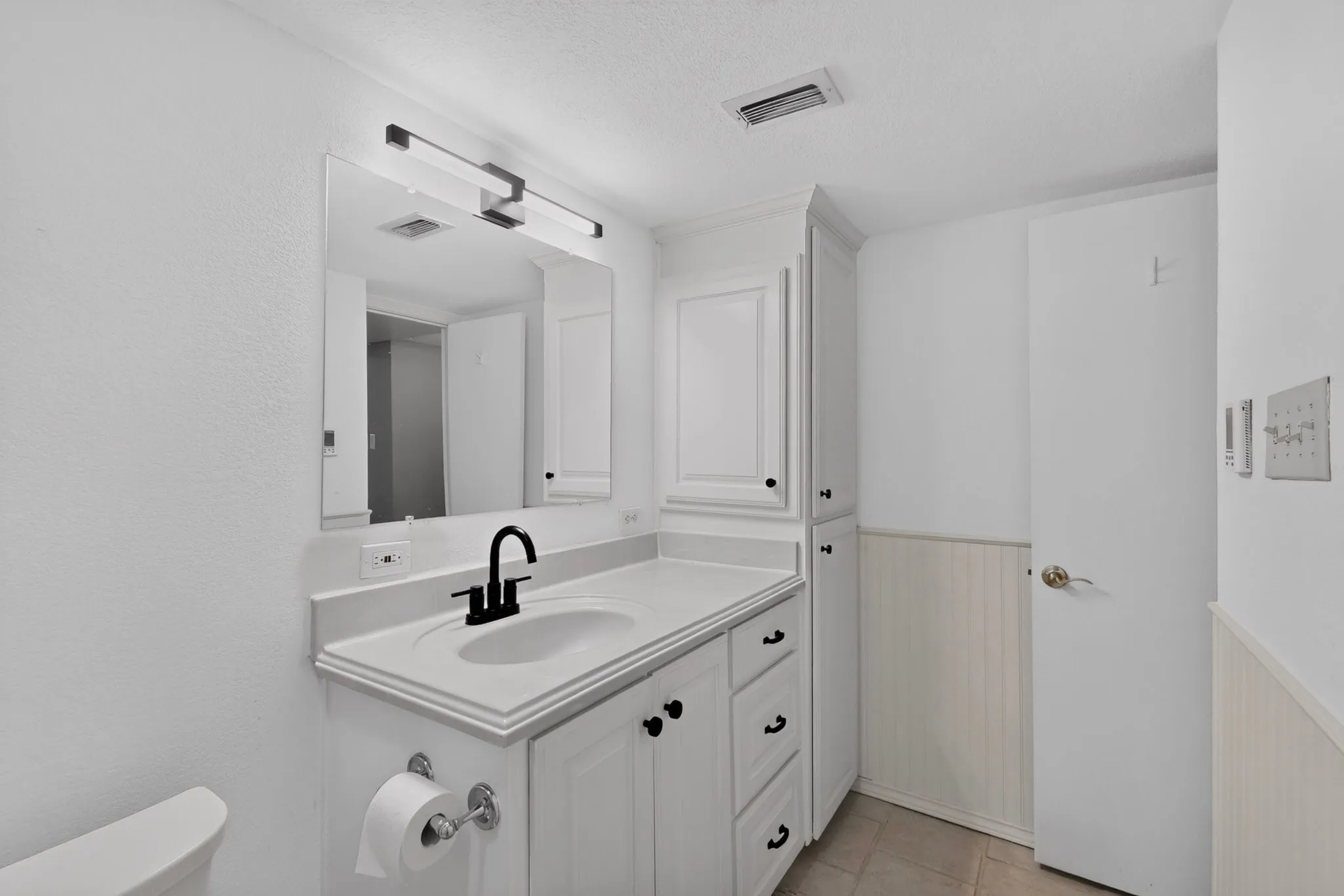White vanity with integrated sink, black hardware, and an overhead light fixture