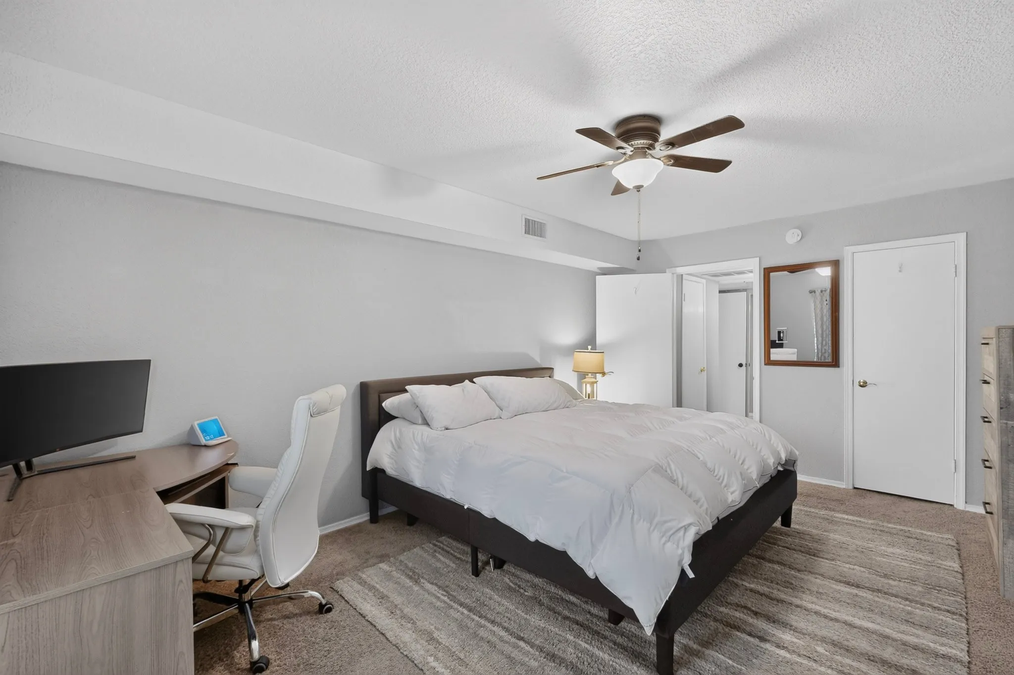 Spacious room featuring neutral grey wall tones, textured carpet flooring, a ceiling fan with integrated lighting, and white interior doors