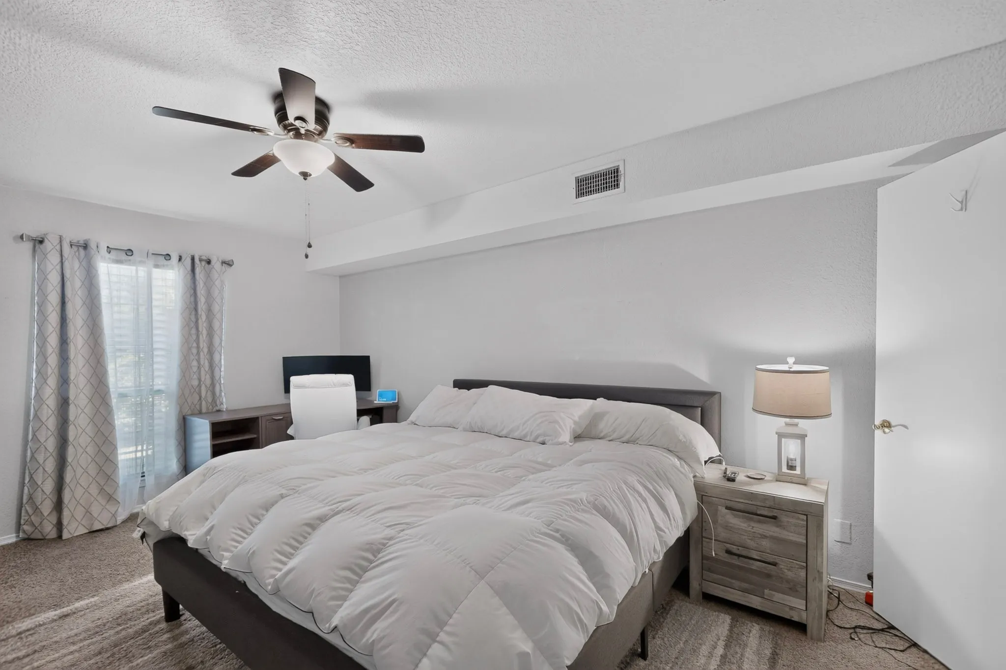 Spacious bedroom featuring light neutral wall paint and textured carpeting