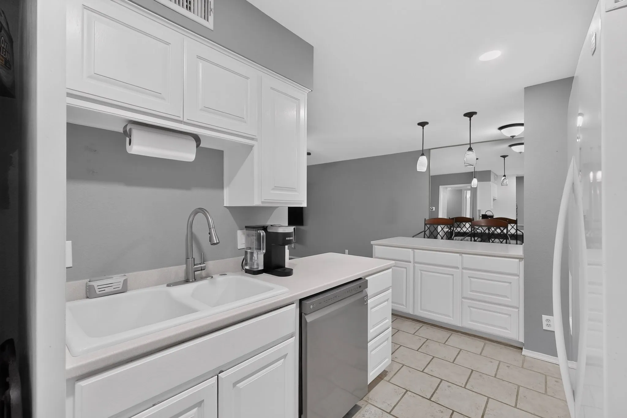 Kitchen featuring white cabinetry, light-toned countertops, a double basin sink with a gooseneck faucet, a stainless steel dishwasher, and tile flooring