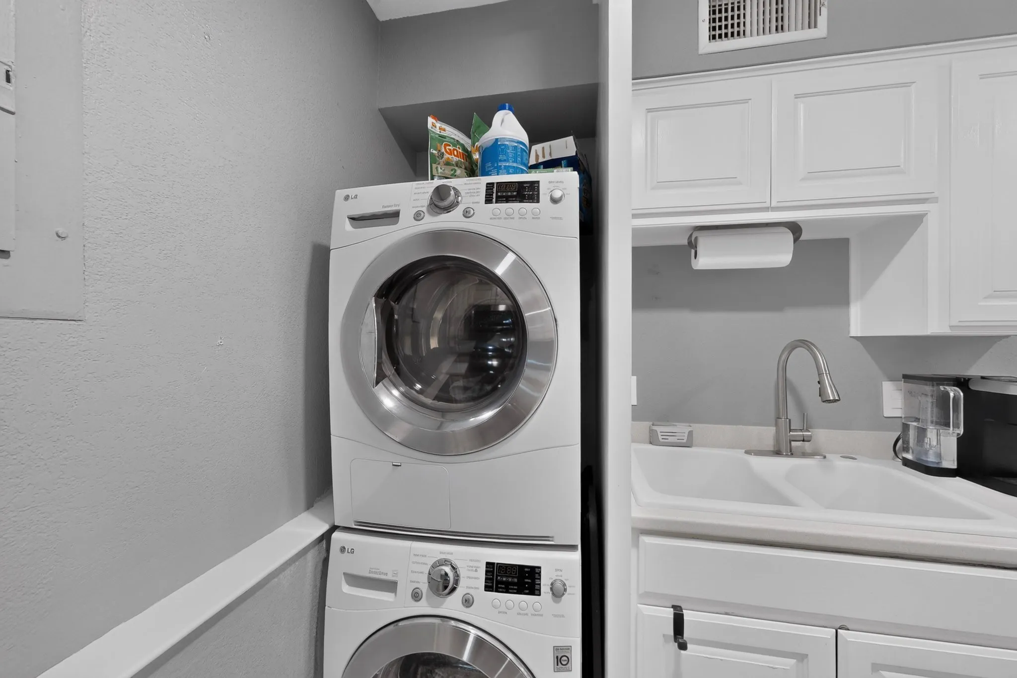 Laundry area featuring a stacked washer and dryer, white shaker-style cabinetry, and a double basin sink with a chrome faucet