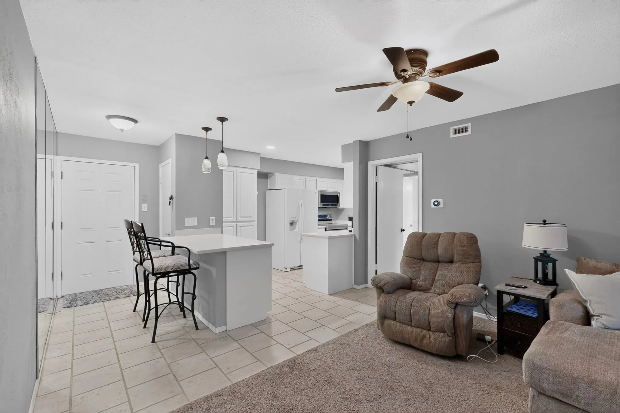 Kitchen and living area featuring tiled flooring, a kitchen island with pendant lighting, white cabinetry, and a ceiling fan