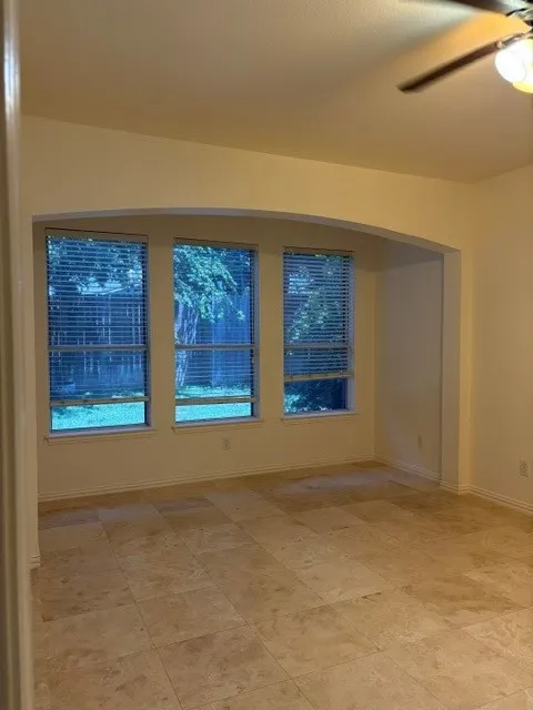 Expansive room featuring large format tile flooring, three large windows with horizontal blinds, a decorative arched doorway, and a ceiling fan with integrated lighting