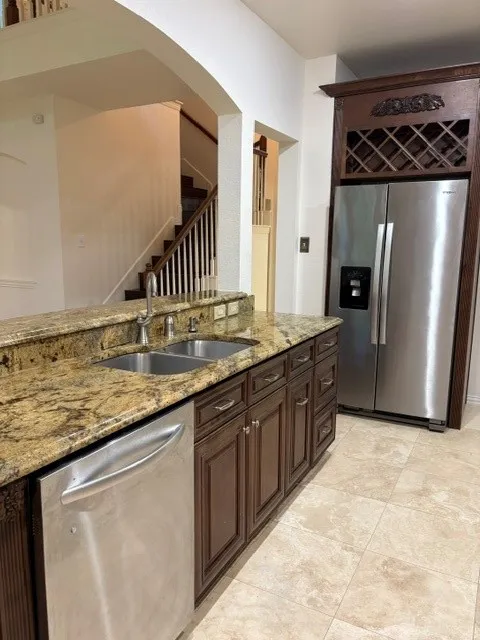 Kitchen island featuring a dual basin sink, stainless steel dishwasher, and stone-finish countertops